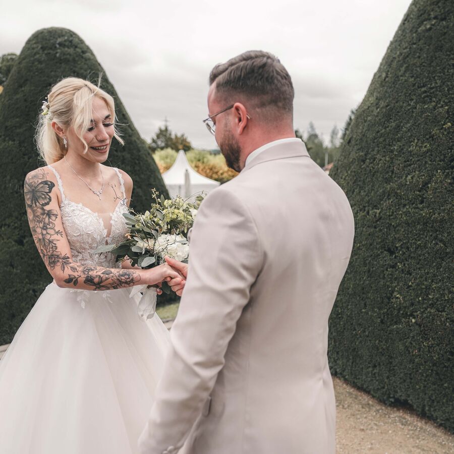 Authentische Hochzeitsfotos: Die Braut mit kunstvollen Tattoos lächelt ihren Bräutigam glücklich beim ersten Aufeinandertreffen vor der Trauung an.