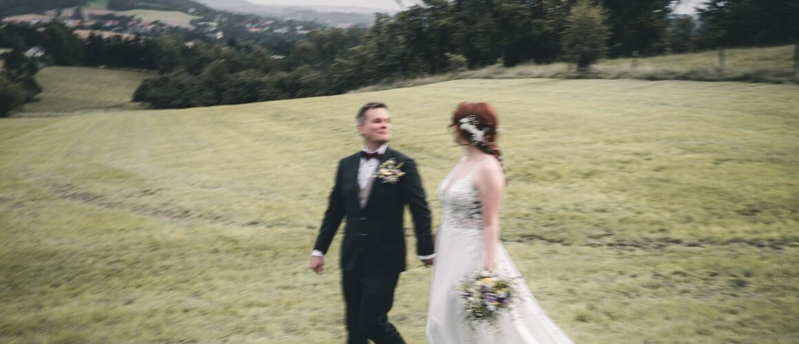 Brautpaar läuft gemeinsam über eine Wiese – natürliche Hochzeitsreportage in Oppach, Sachsen