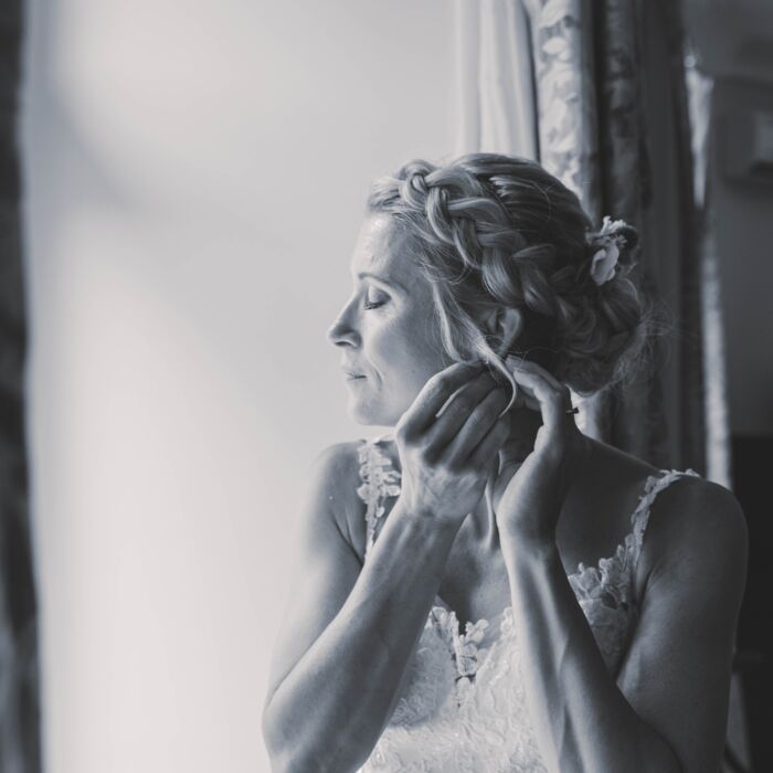 Braut am Fenster beim einfädeln Ihrer Ohrringe, Hochzeit im Schlosshotel Schkopau