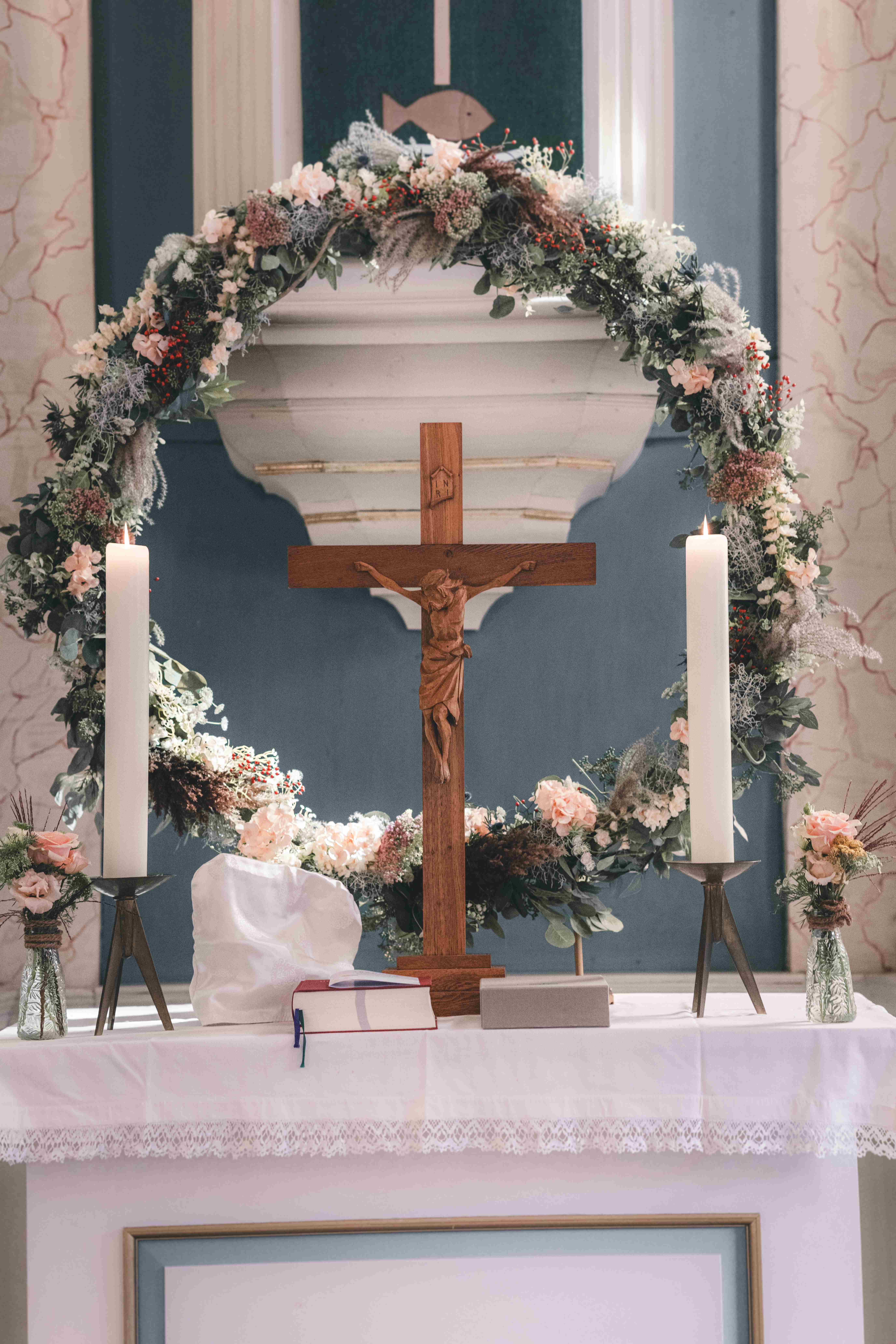 Ein wunderschön mit Trockenblumen geschmückter Altar mit einem großen runden Blumenbogen, zwei Kerzen und einem hölzernen Kruzifix.