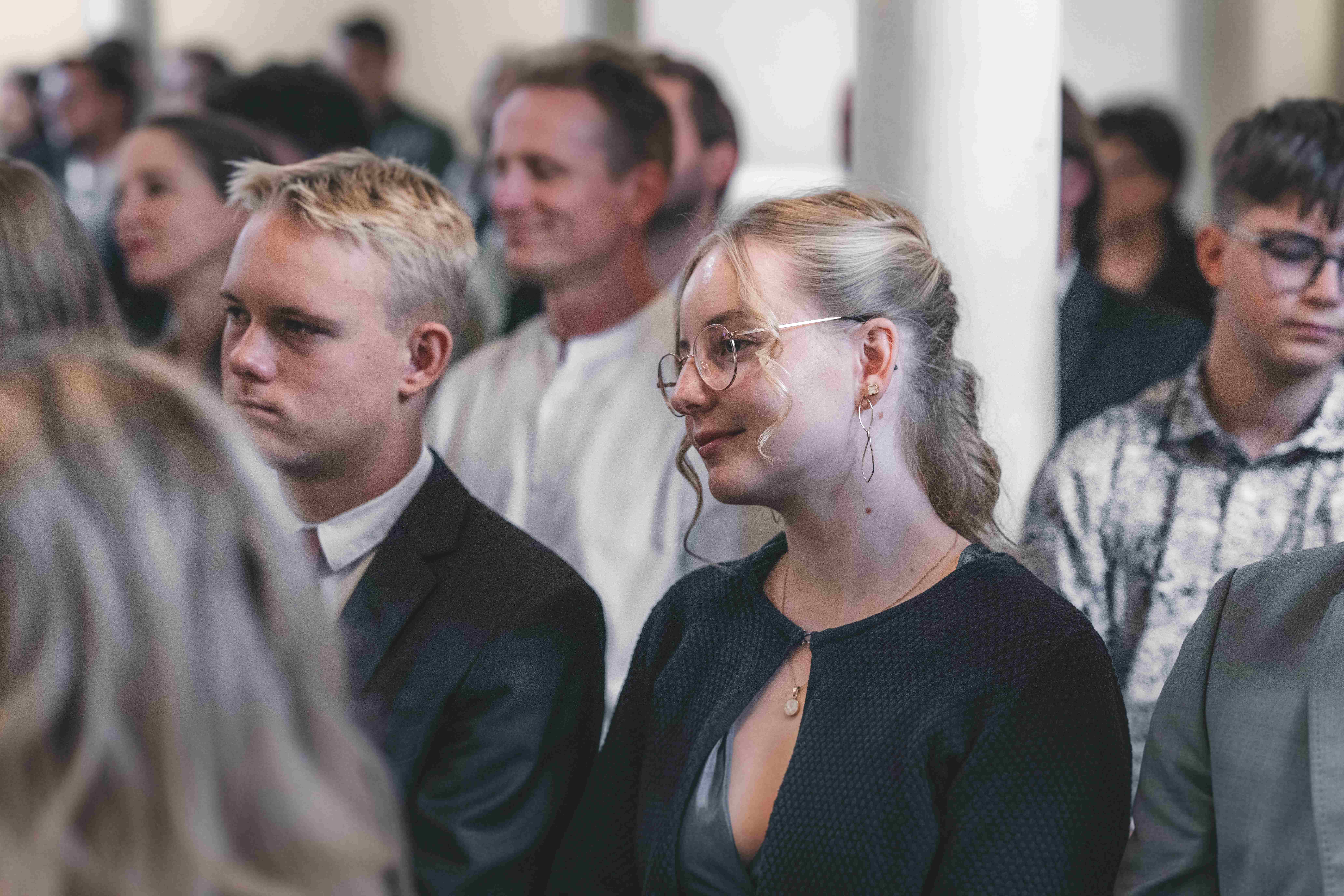 Eine junge Hochzeitsgästin mit Brille und hochgesteckten Haaren lauscht mit einem sanften Lächeln der Predigt in der Kirche Leisnig.
