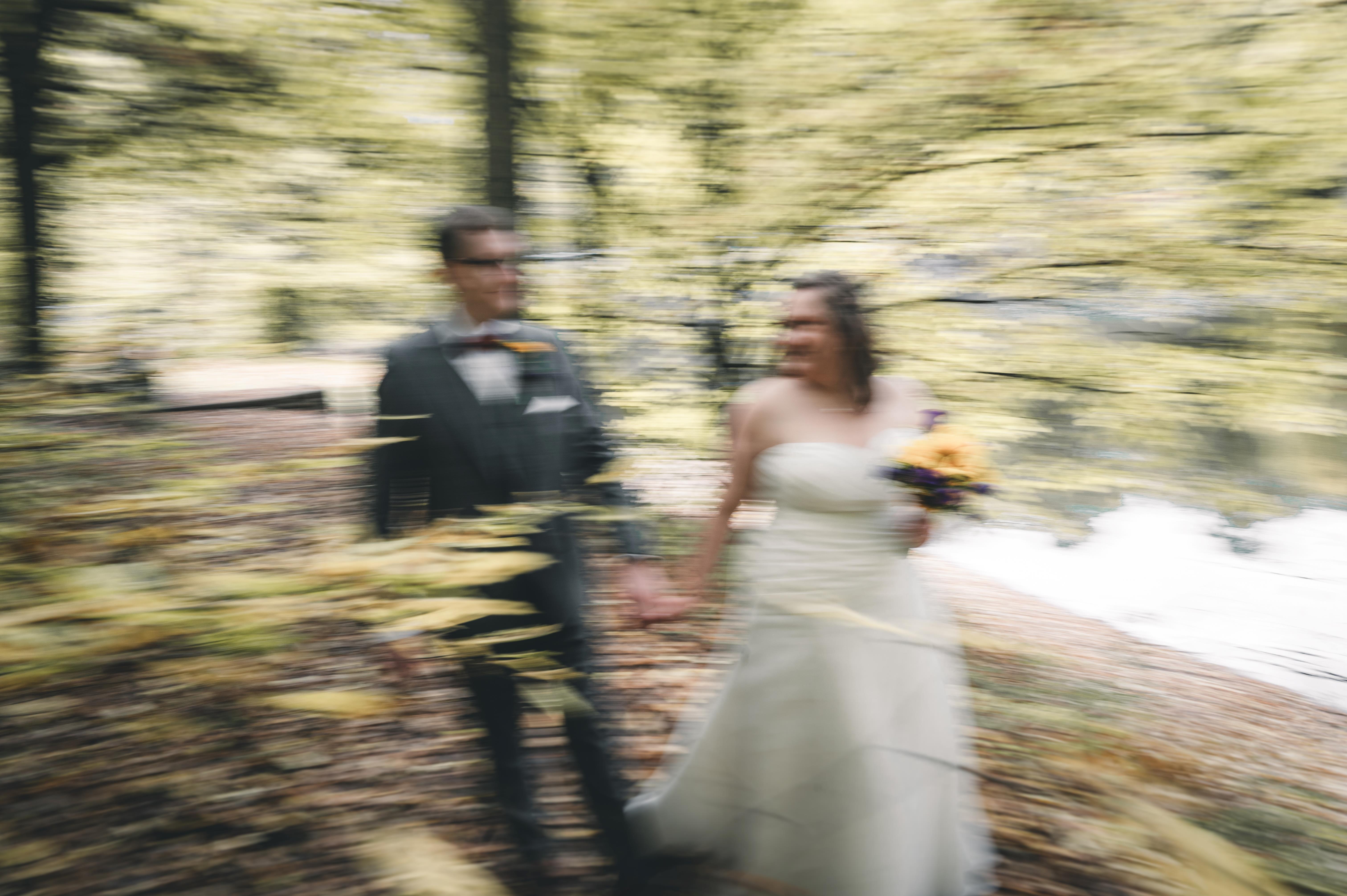 Künstlerische Aufnahme mit Bewegungsunschärfe (Motion Blur): Das Brautpaar läuft Hand in Hand glücklich einen Waldweg in Coswig bei Dresden entlang.