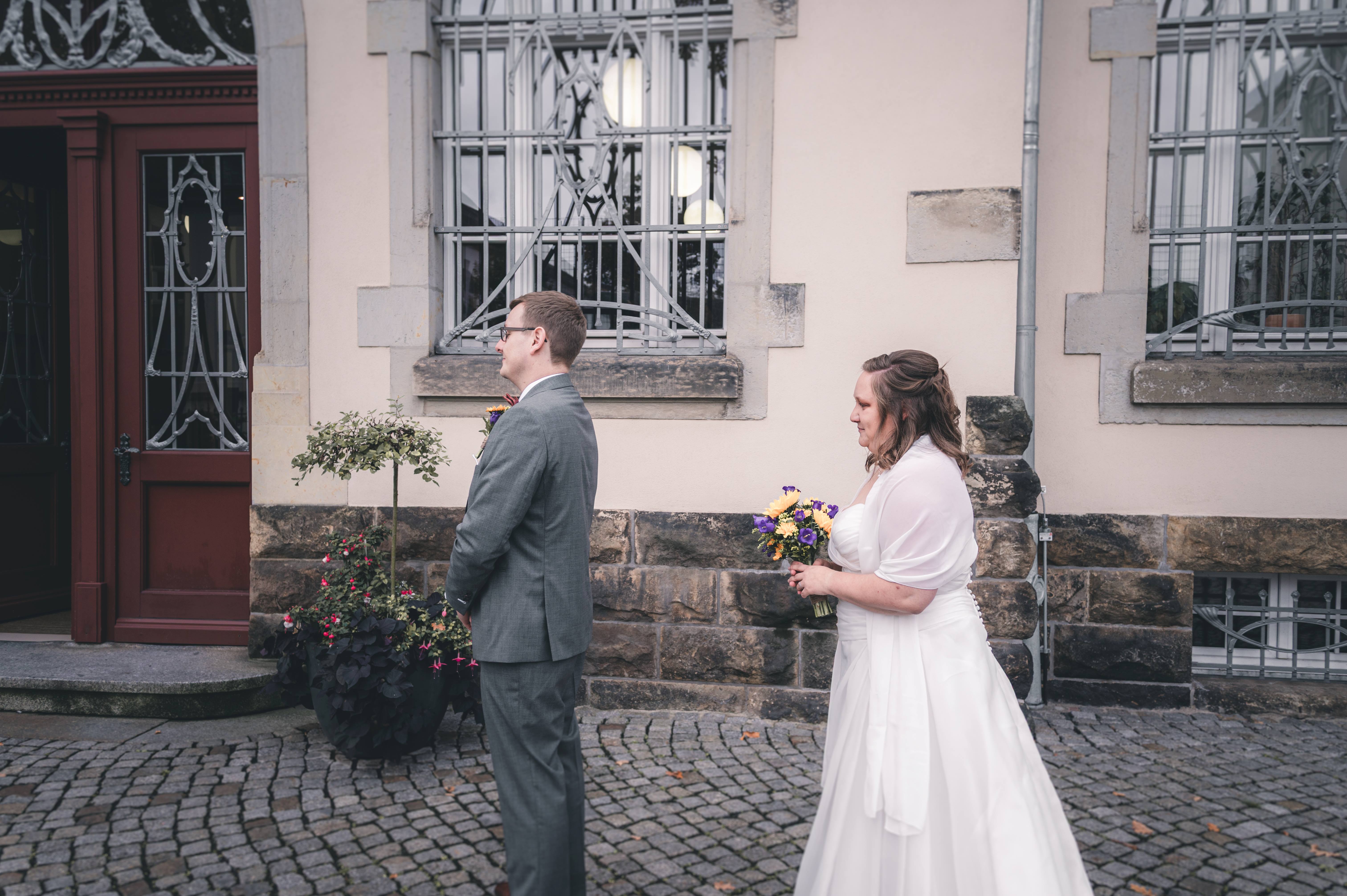 Die Braut läuft mit ihrem Sonnenblumen-Brautstrauß auf ihren Bräutigam zu, der vor dem Eingang des Standesamtes Radebeul wartet.