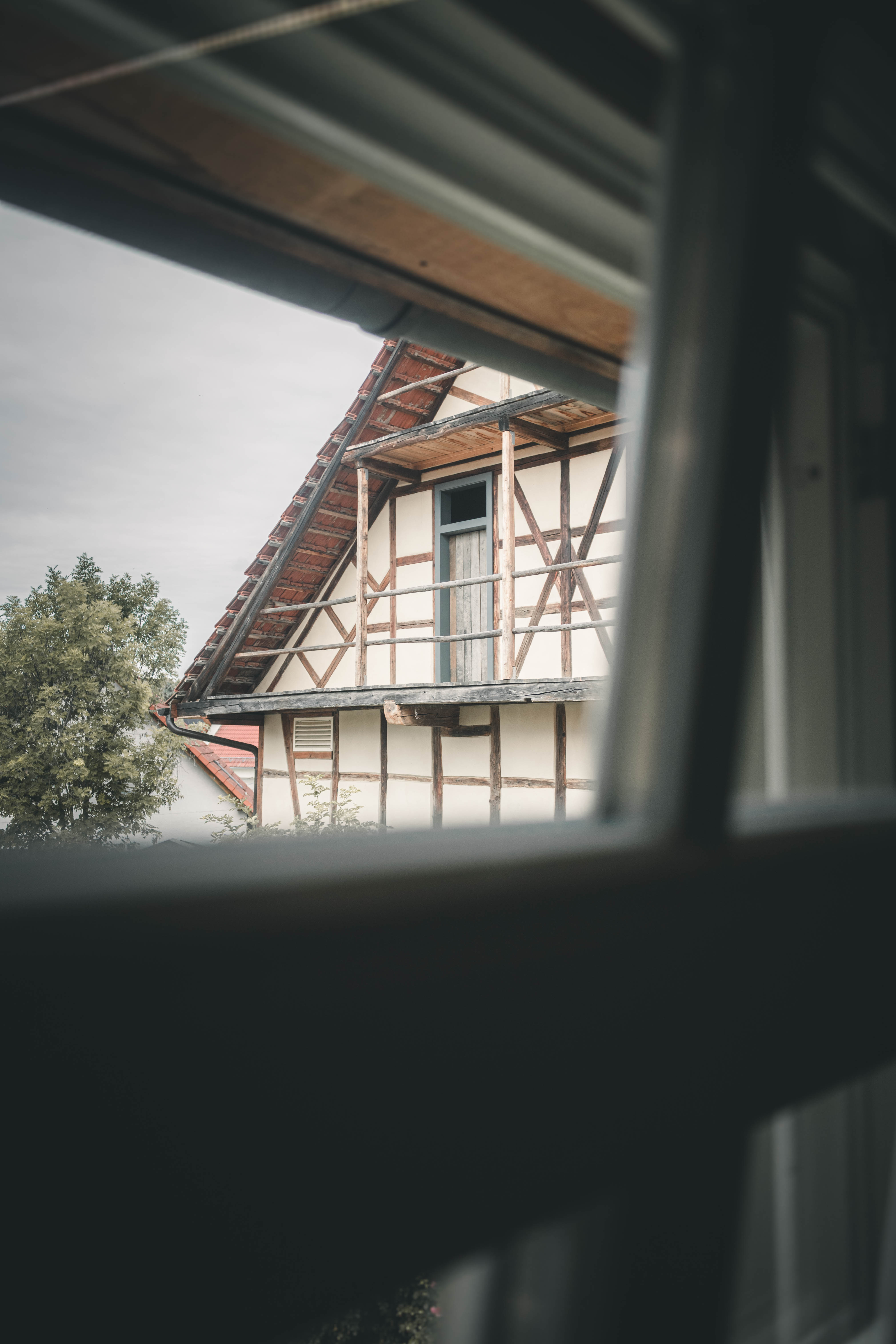 Blick durch das Fensterrahmen auf das traditionelle Fachwerkgebäude und den hölzernen Balkon des Magdalenenguts Erfurt.