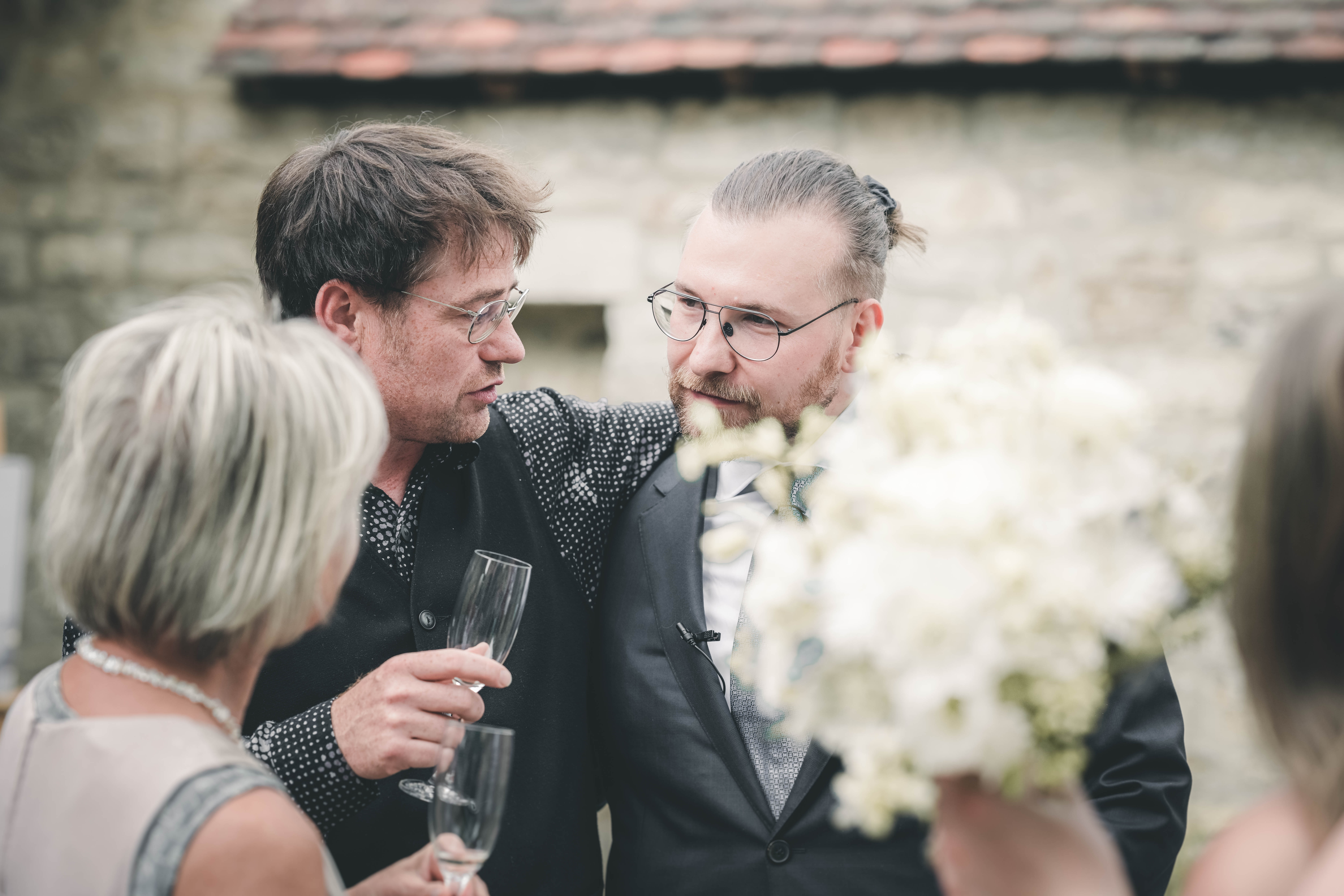 Der Bräutigam mit Brille und Ansteckblume im intensiven, lachenden Gespräch mit Gästen und Freunden im Magdalenengut Erfurt.