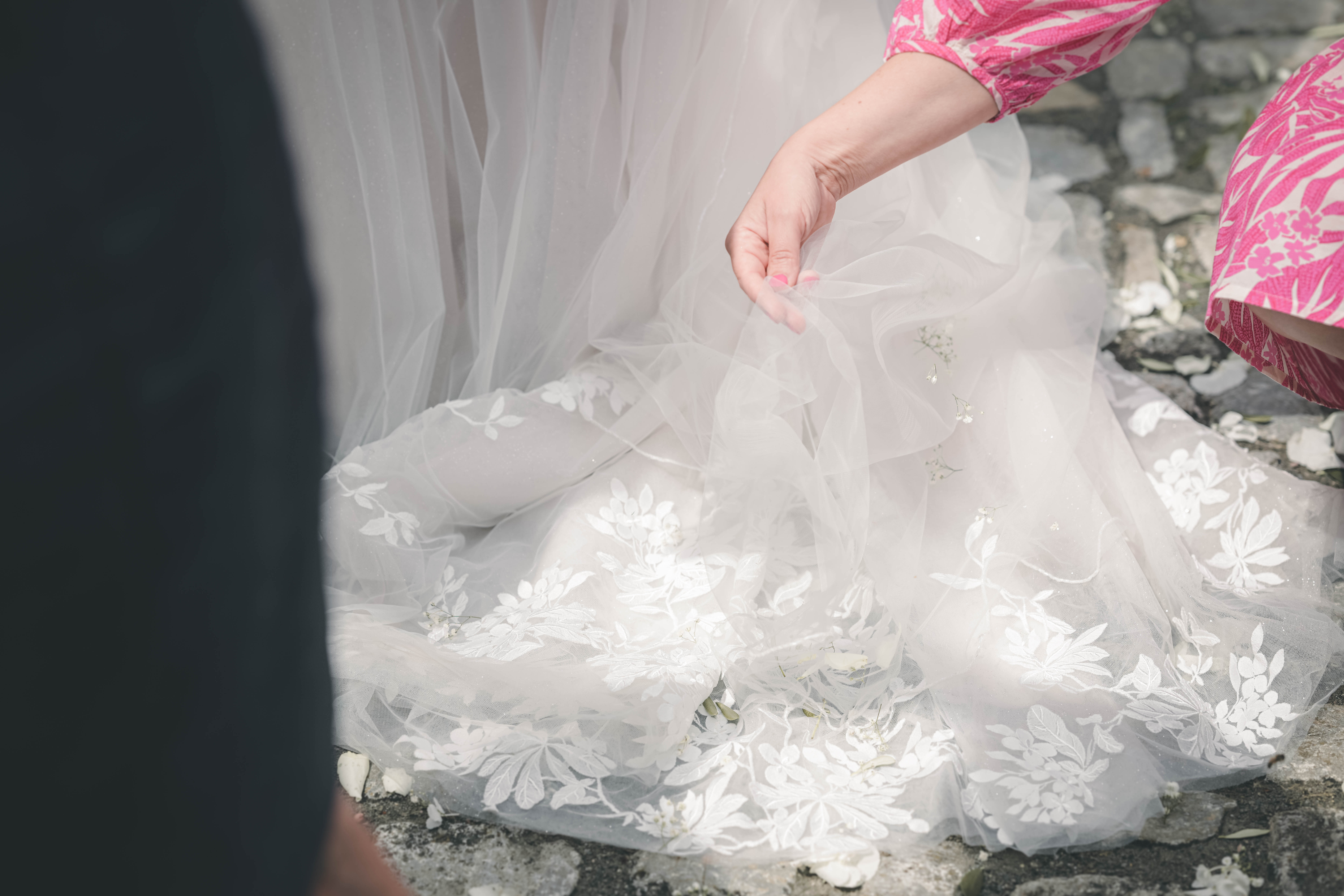 Nahaufnahme der Tüllschleppe des Brautkleids mit floralen Spitzenapplikationen und weißen Blütenblättern auf dem Kopfsteinpflaster im Magdalenengut Erfurt.
