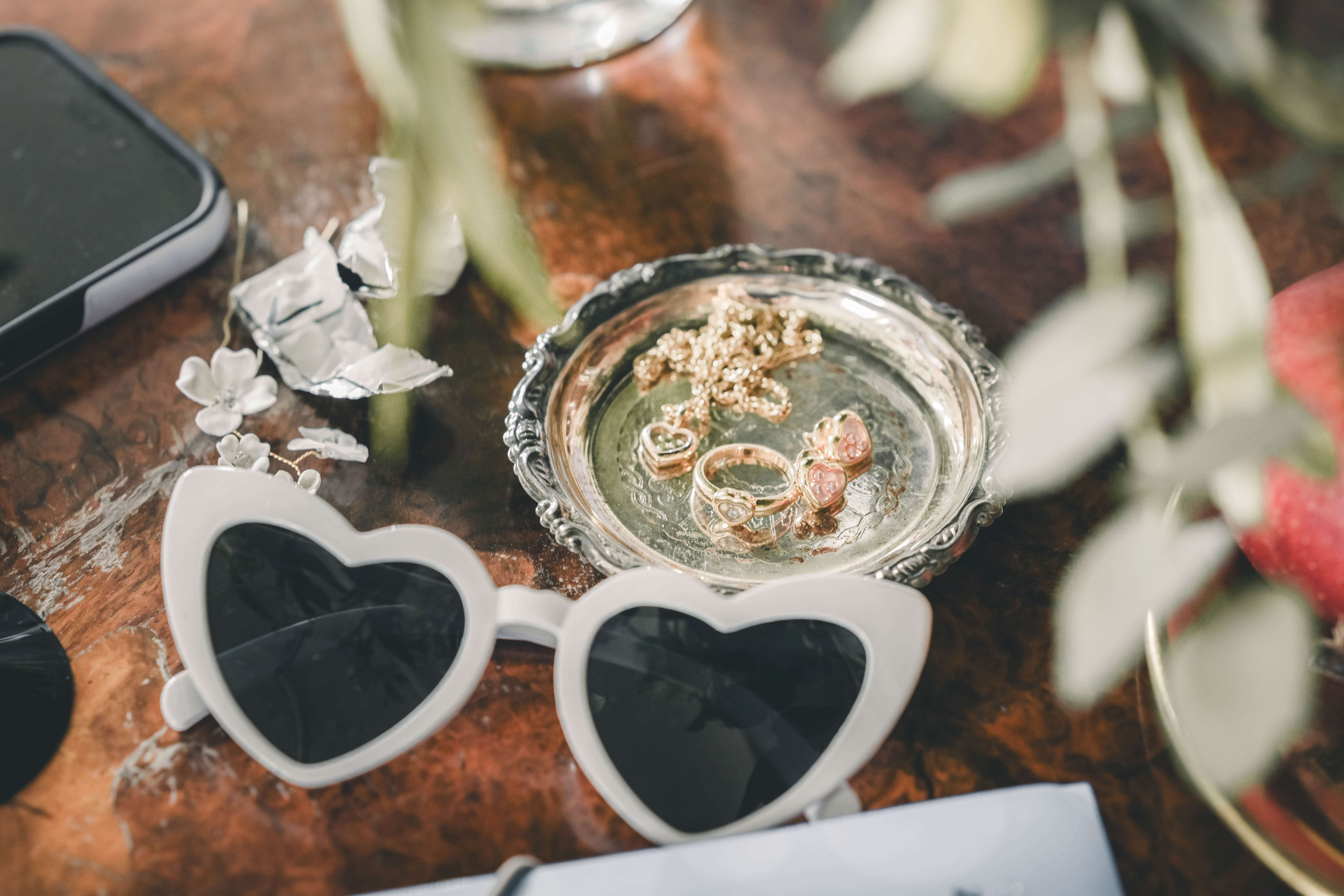Weiße Herz-Sonnenbrille und goldener Brautschmuck mit Ringen und Kette auf einer kleinen verzierten Silberschale im Magdalenengut Erfurt.