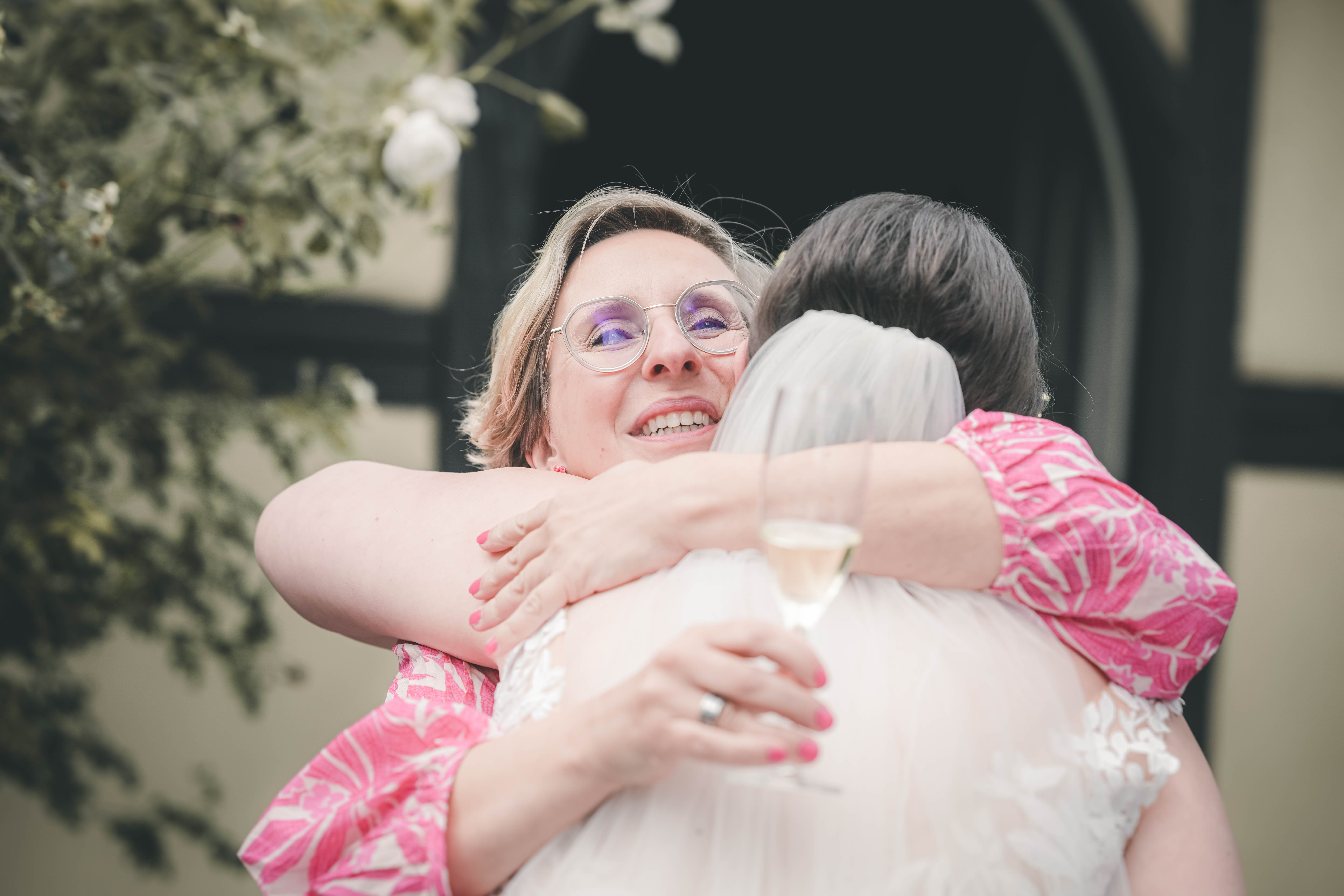 Eine strahlende Dame mit Brille im pinken Kleid umarmt die Braut herzlich während des Sektempfangs im Magdalenengut Erfurt.