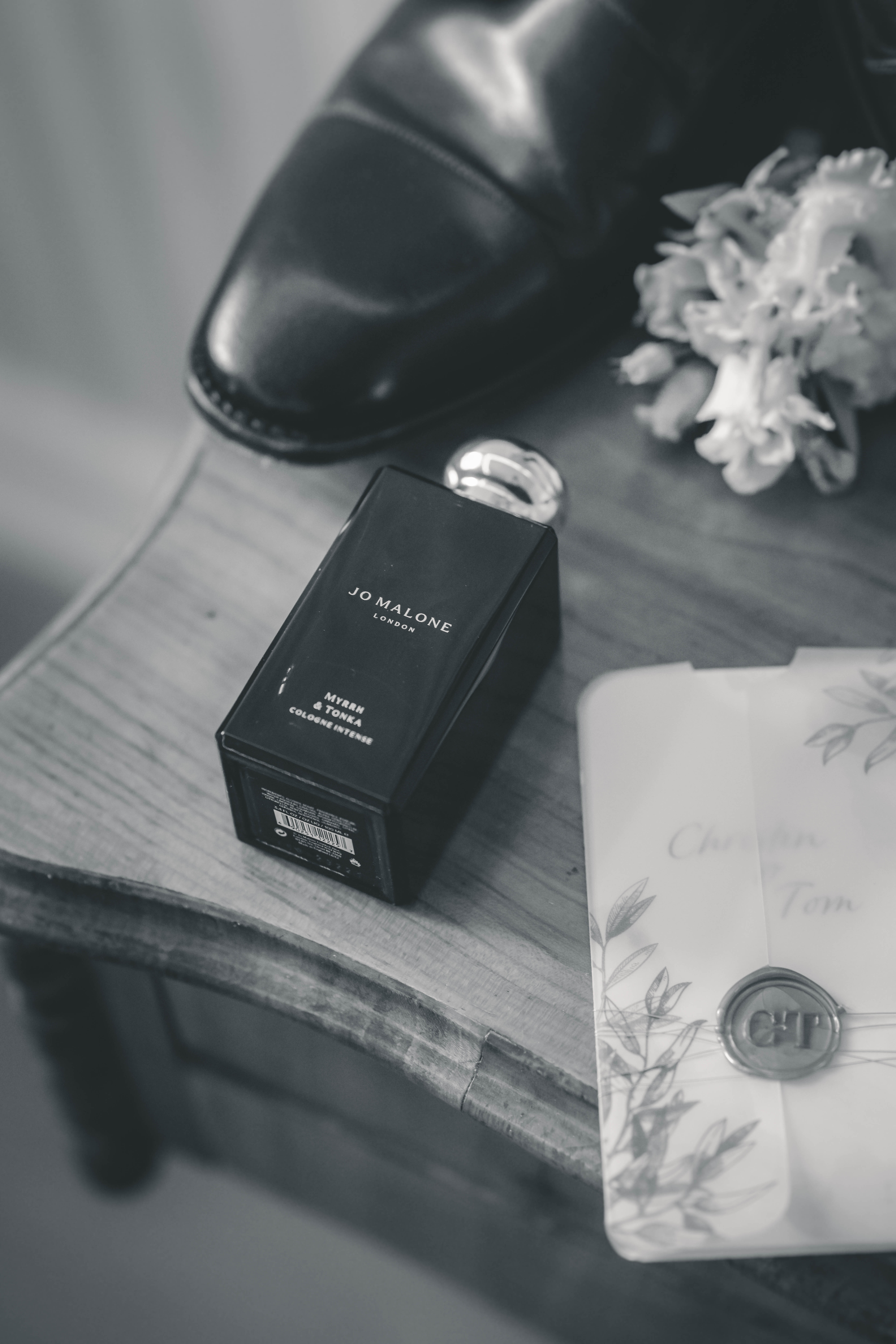 Schwarz-Weiß-Aufnahme eines Jo Malone Flakons neben einer Hochzeitseinladung mit personalisiertem Wachssiegel.