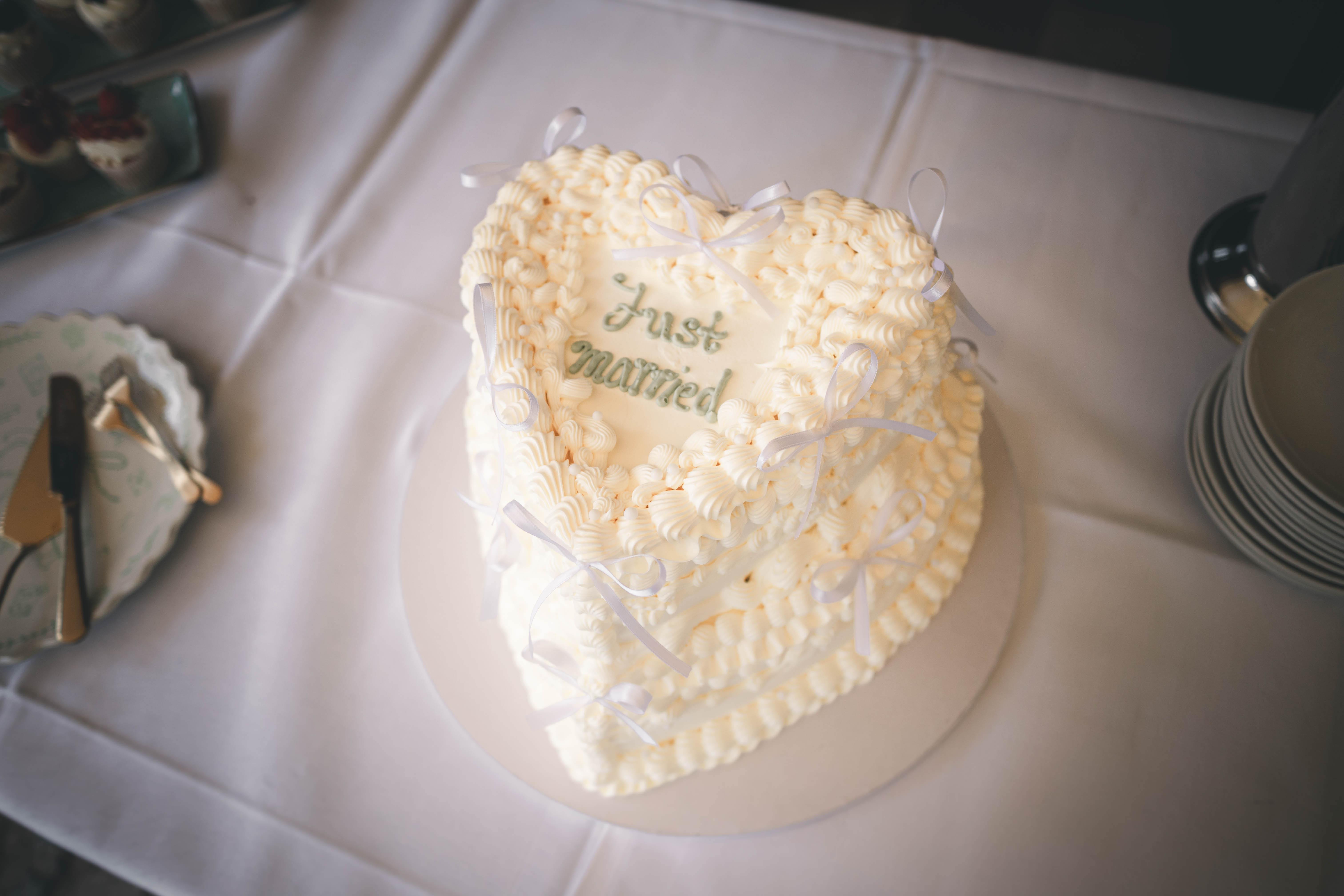 Weiße, herzförmige Hochzeitstorte im Vintage-Stil mit Rüschen-Cremeverzierung, kleinen Schleifen und grünem „Just Married“-Schriftzug im Magdalenengut Erfurt.