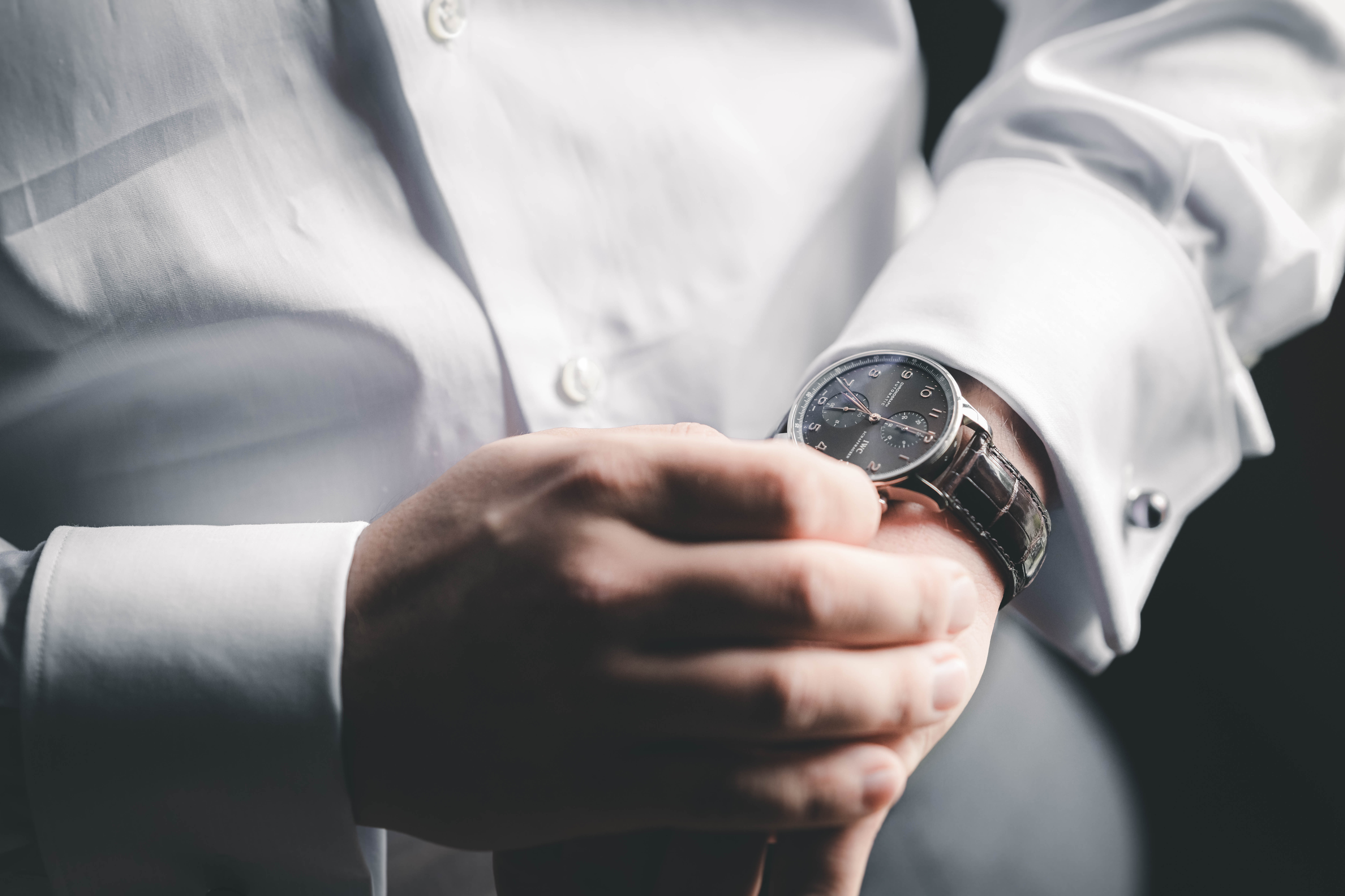 Makroaufnahme des Bräutigams mit weißer Doppelmanschette, silbernem Manschettenknopf und eleganter IWC-Uhr mit Lederarmband.