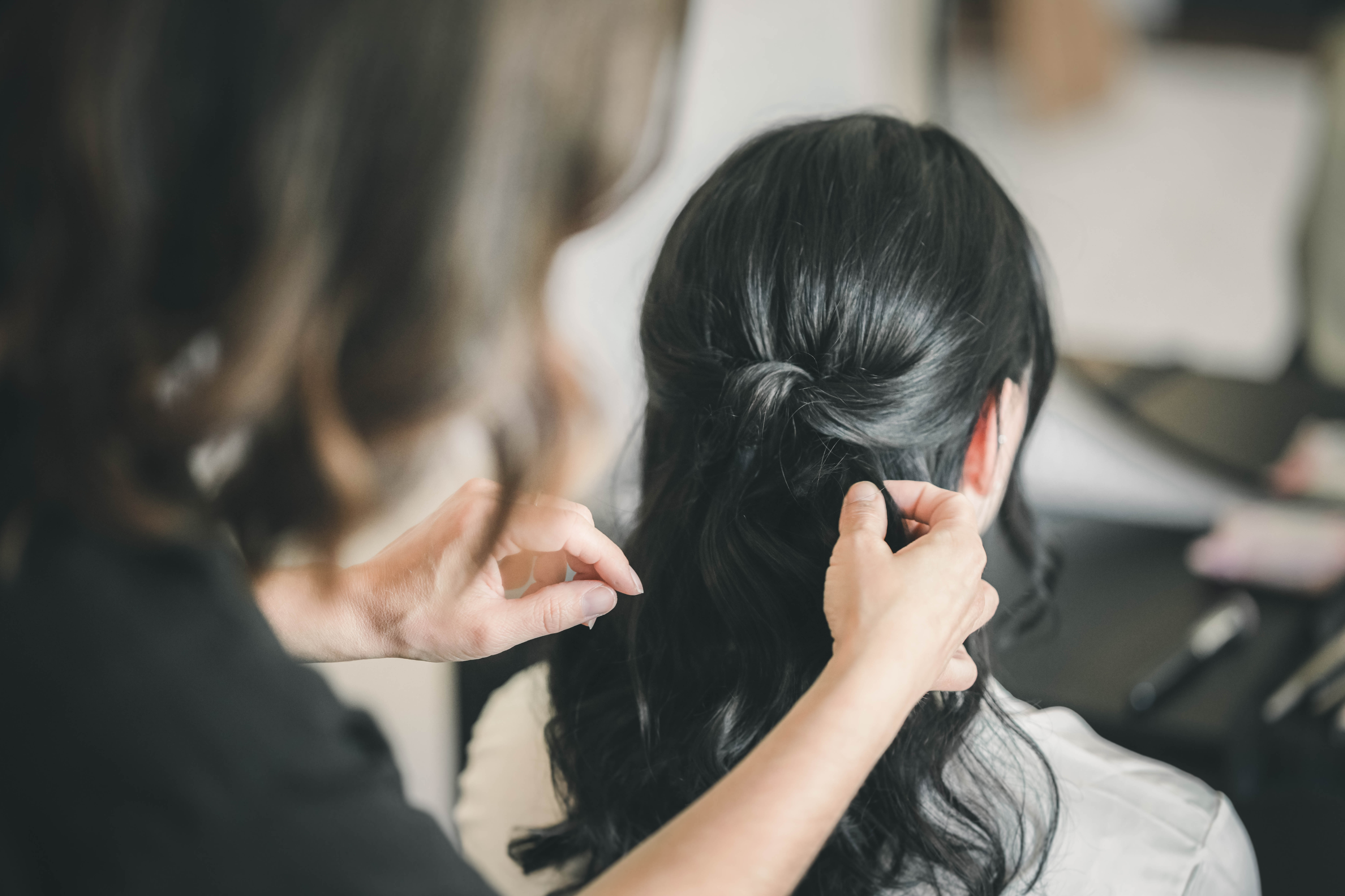 Nahaufnahme, wie die Hände der Stylistin die dunklen, gelockten Haare der Braut zu einer eleganten Hochzeitsfrisur stecken.