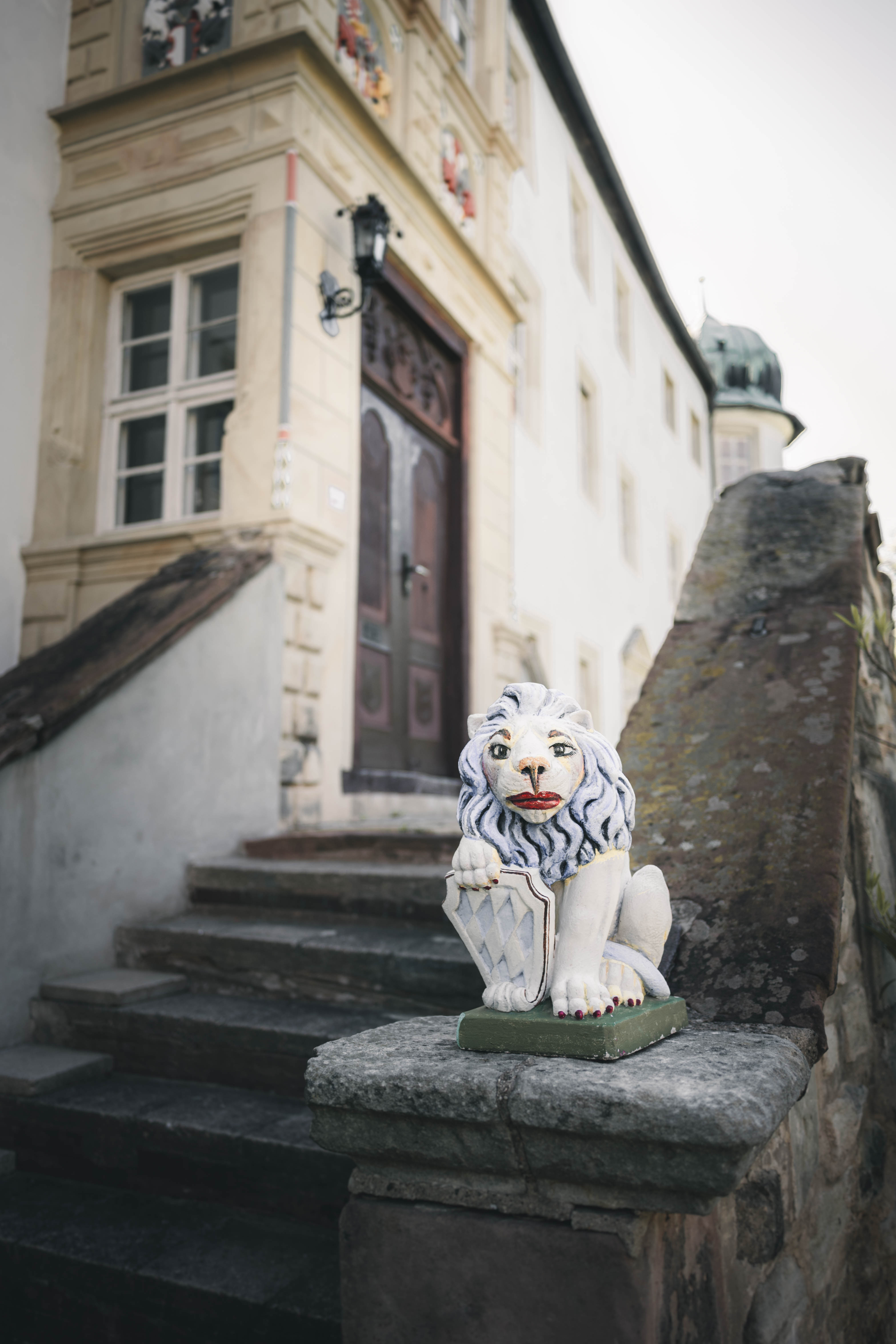 Eine steinerne Löwenwappen-Figur bewacht die historische Steintreppe, die zum prachtvollen hölzernen Eingangsportal des Schlosses Frankleben führt.