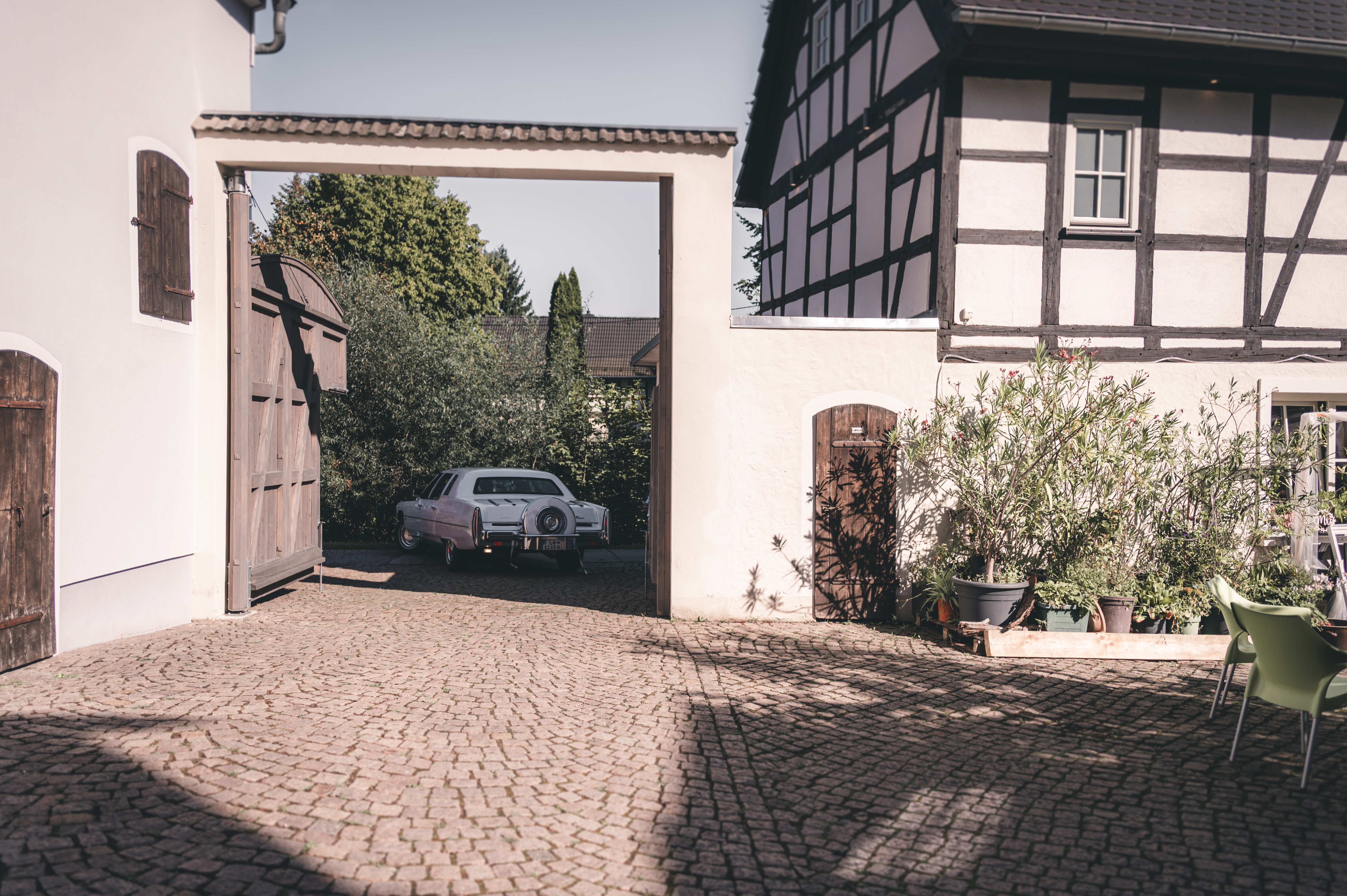 Das weiße Hochzeitsauto parkt elegant im kopfsteingepflasterten Innenhof des Erlebnishofs Pleißental in Fraureuth.