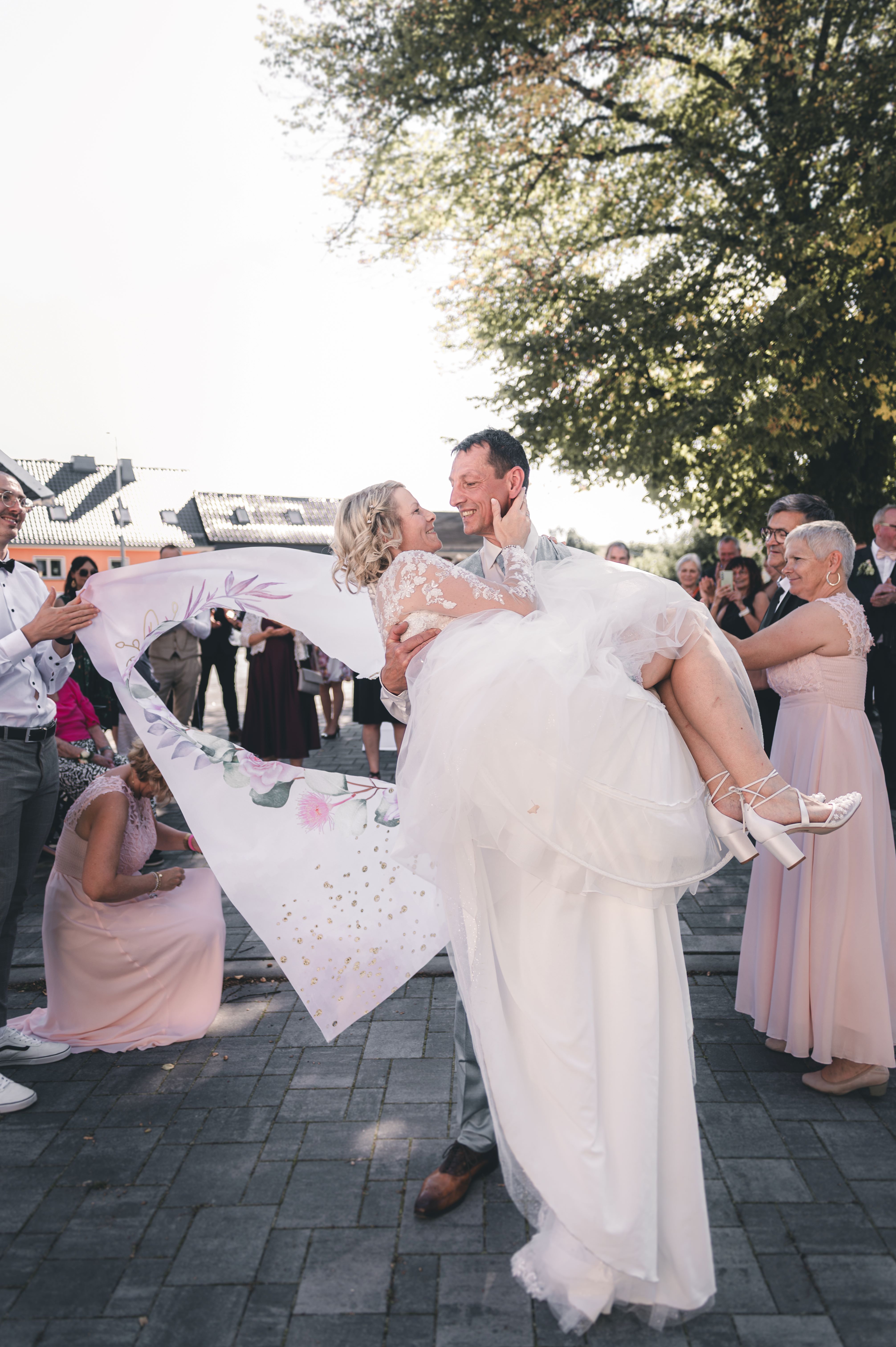 Steffen hält seine Kristina im Brautkleid auf den Armen und küsst sie innig inmitten der jubelnden Hochzeitsgäste im Erzgebirge.