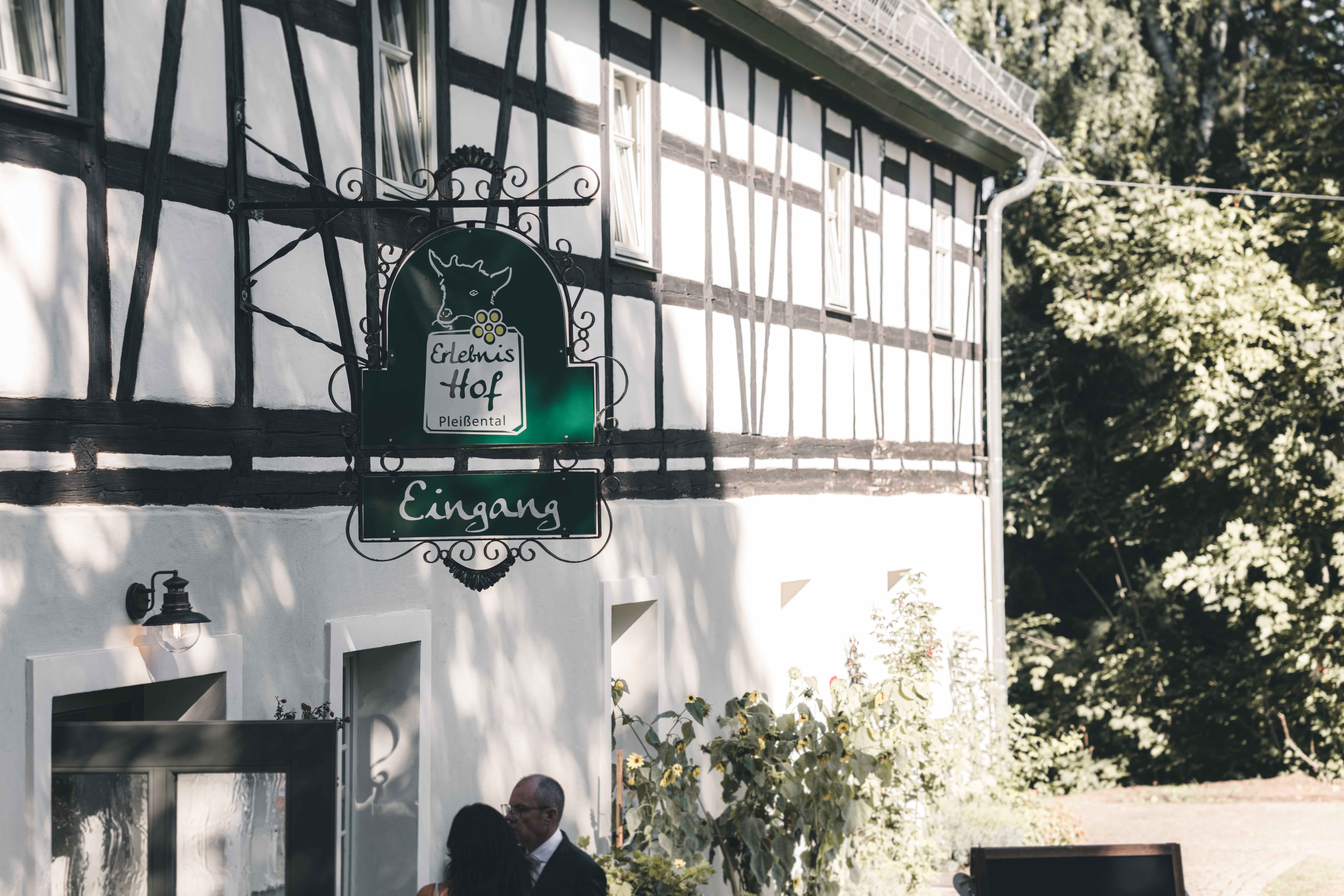Das geschmiedete grüne Eingangsschild des Erlebnishofs Pleißental an der weißen Fachwerkwand während einer Hochzeitsfeier im Raum Zwickau.