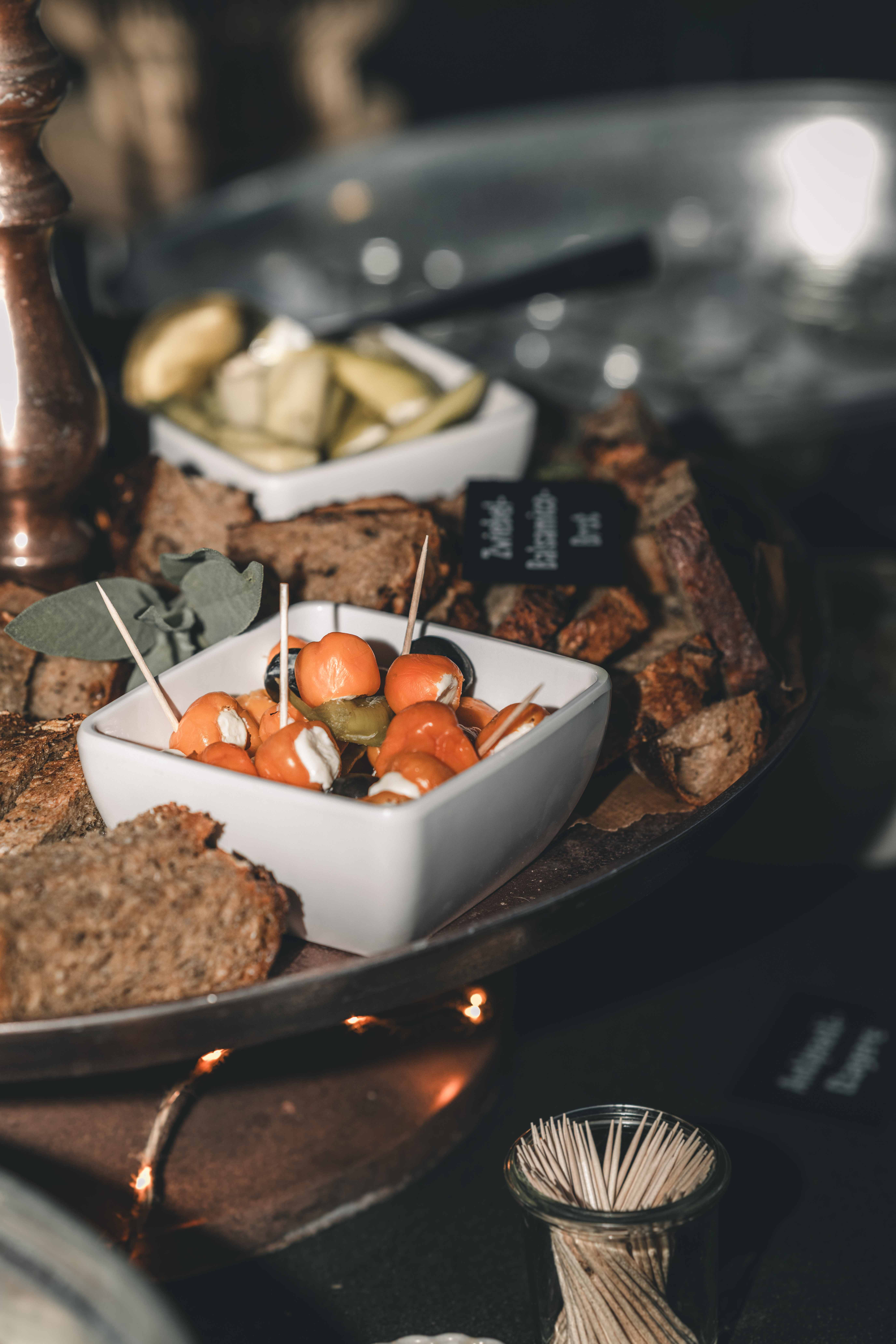 Eine Schale mit gefüllten, orangefarbenen Paprikaschoten auf Spießen und frisches Zwiebel-Balsamico-Brot auf dem Hochzeitsbuffet.