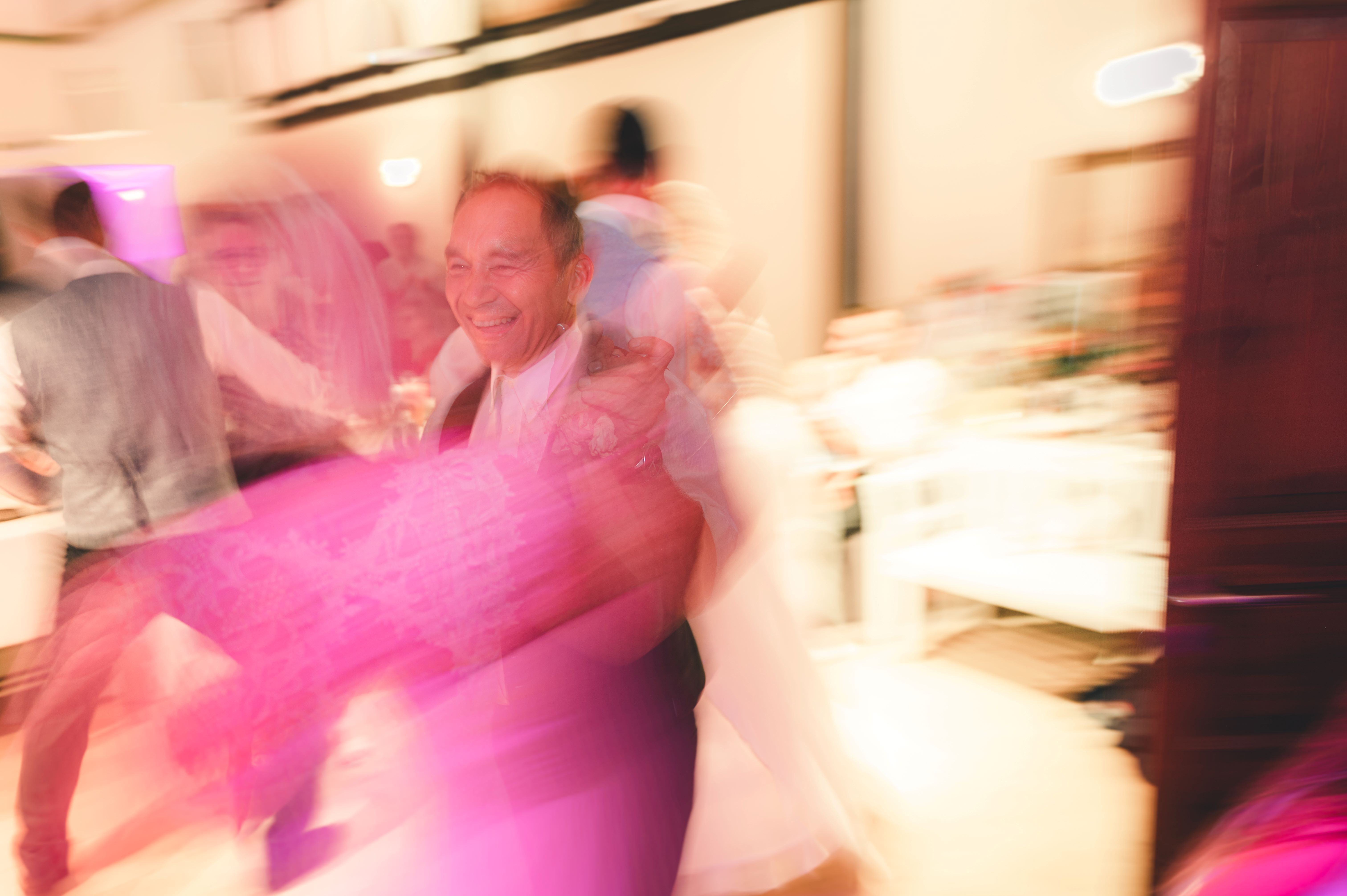 Ein dynamisches Partyfoto mit bunter Beleuchtung zeigt einen älteren, glücklich lachenden Gast beim ausgelassenen Tanzen im Erzgebirge.