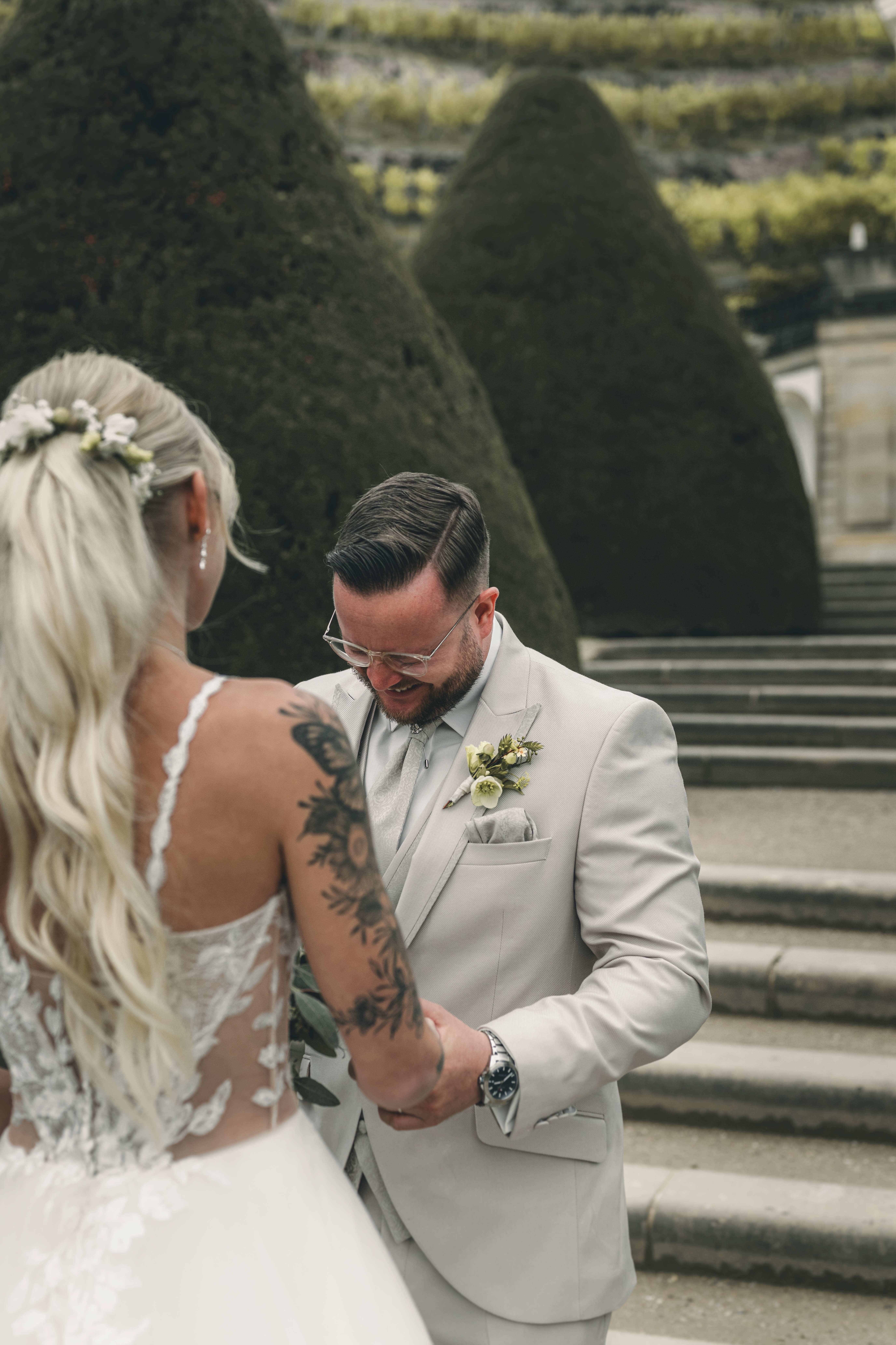 Der Bräutigam blickt seine Braut beim First Look auf Schloss Wackerbarth ergriffen an, während er ihre Hände hält. Im Hintergrund sind die Hecken zu sehen.