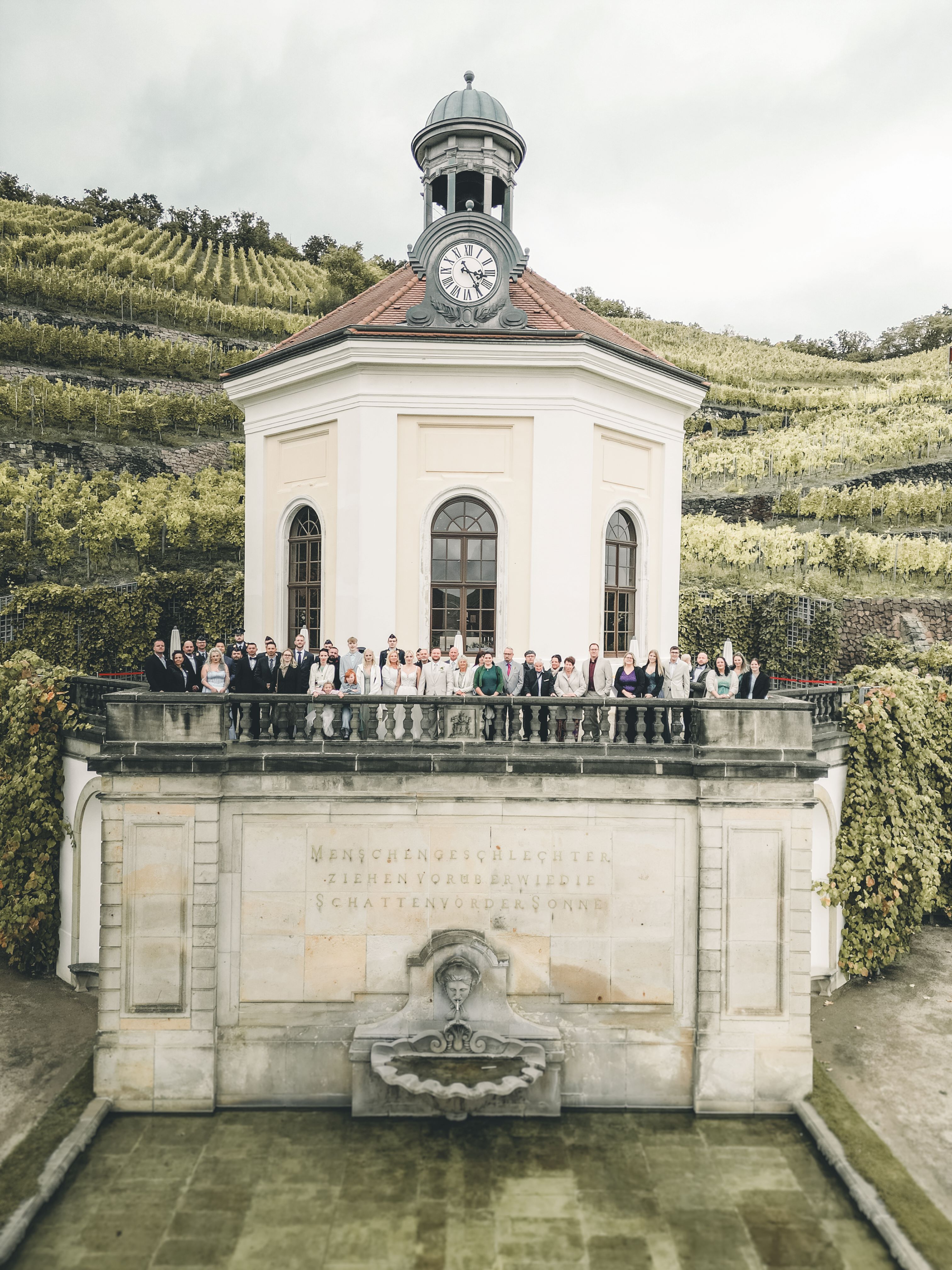 Eine beeindruckende Aufnahme der gesamten Hochzeitsgesellschaft, die für ein großes Gruppenfoto auf der Balustrade des historischen Belvedere-Pavillons auf Schloss Wackerbarth posiert.