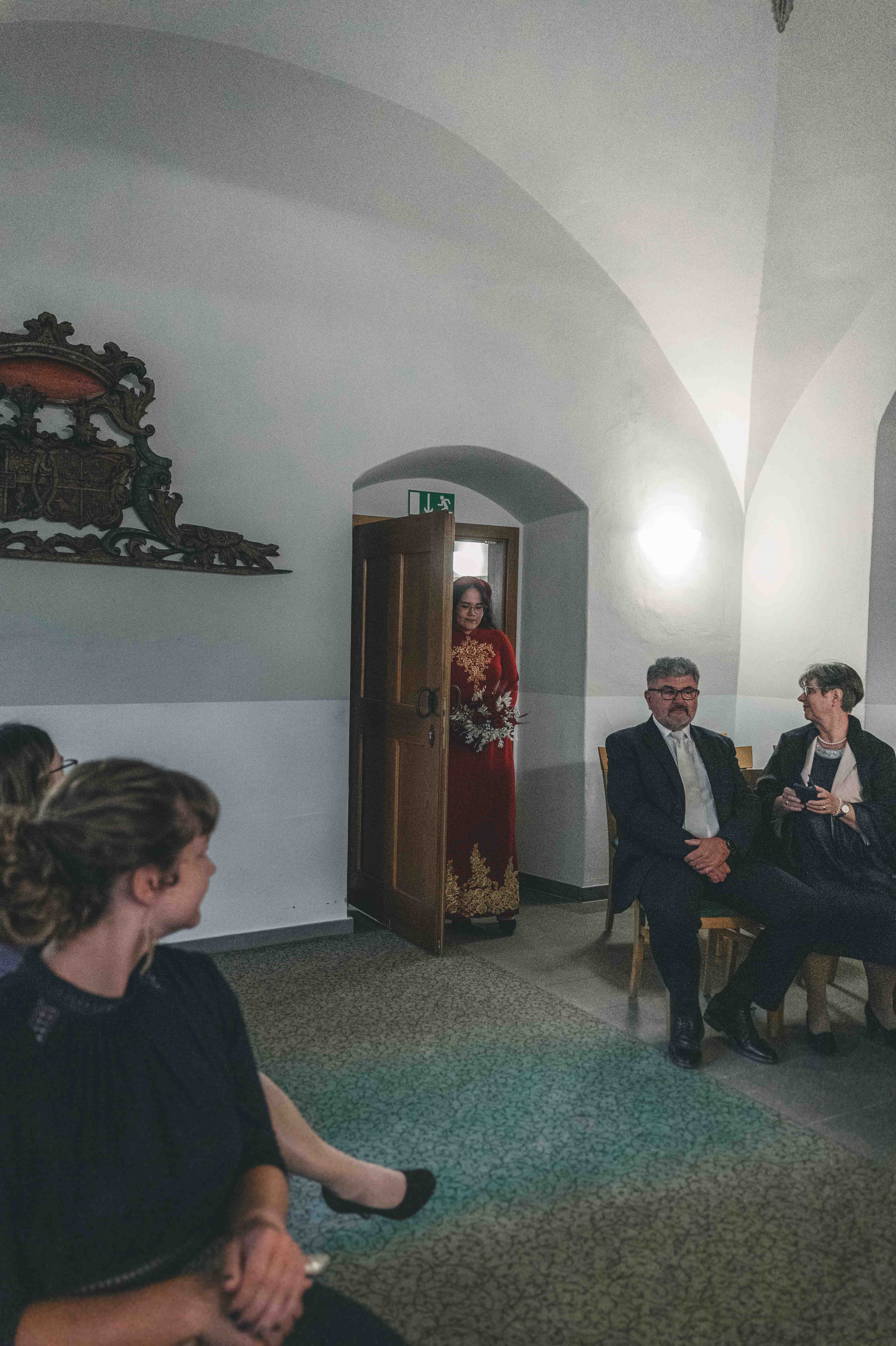 Die Braut im roten traditionellen Kleid öffnet die Holztür und betritt den historischen, gewölbten Trausaal von Schloss Klaffenbach unter den Blicken der Gäste.