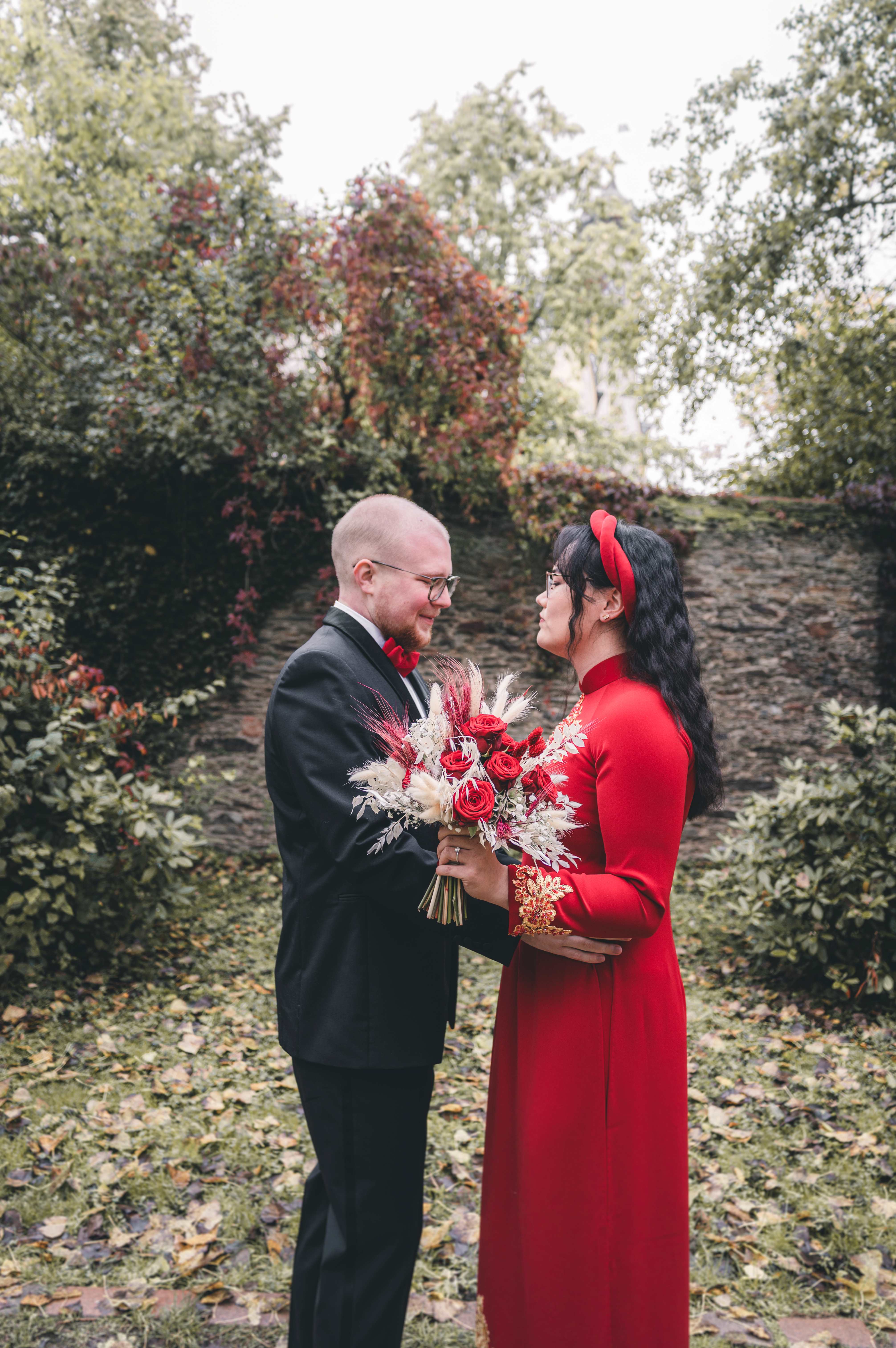 Patrick und Mai Linh blicken sich beim First Look glücklich in die Augen, die Braut trägt ein rotes vietnamesisches Kleid und hält ihren rot-weißen Strauß.