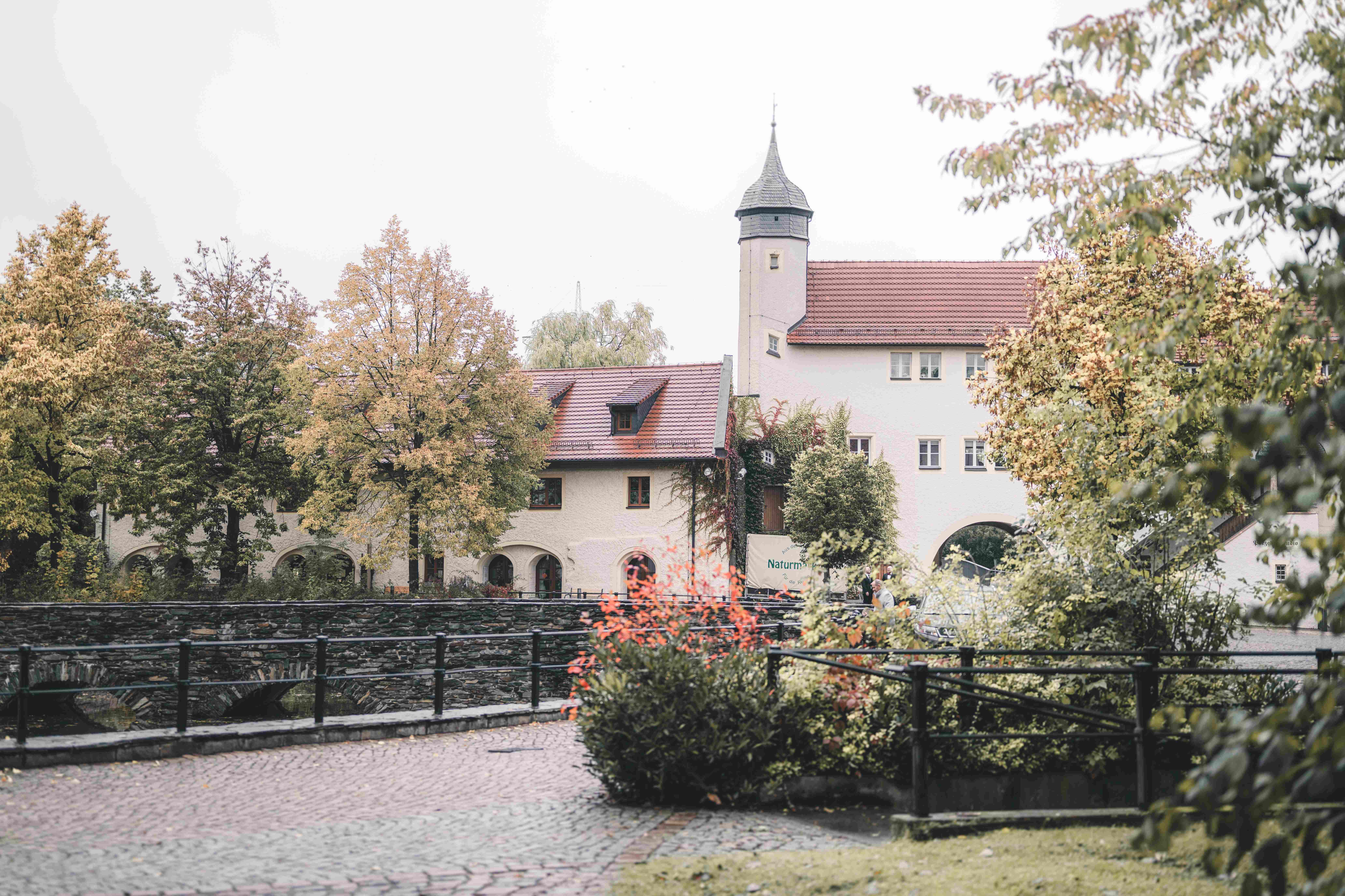 Außenansicht der historischen Gebäude und Brücken von Wasserschloss Klaffenbach bei Chemnitz, umgeben von herbstlichen Bäumen.