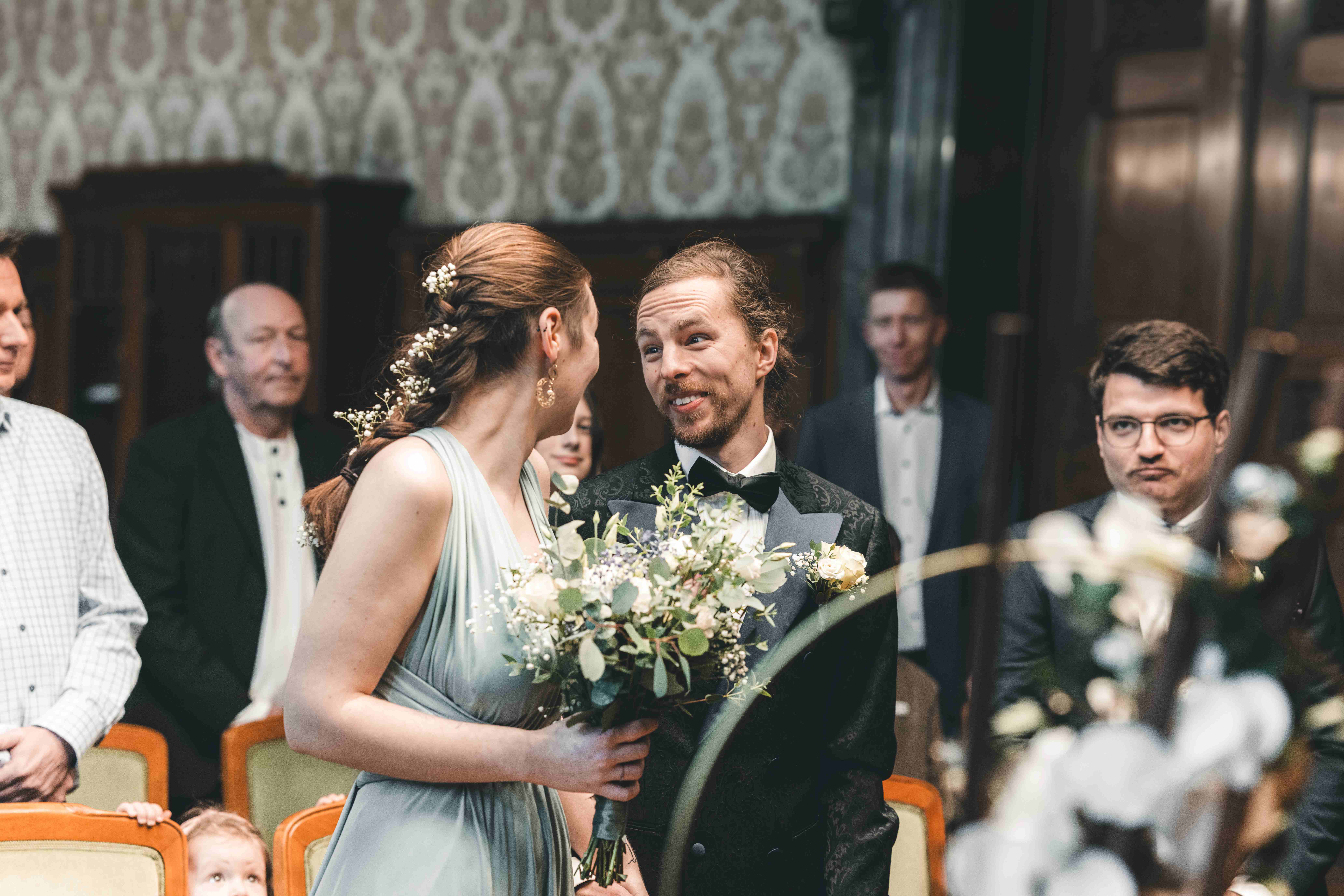 Das Brautpaar blickt sich direkt nach dem Hochzeitskuss im Ratsplenarsaal Leipzig glücklich an, während im Hintergrund die Hochzeitsgäste applaudieren.