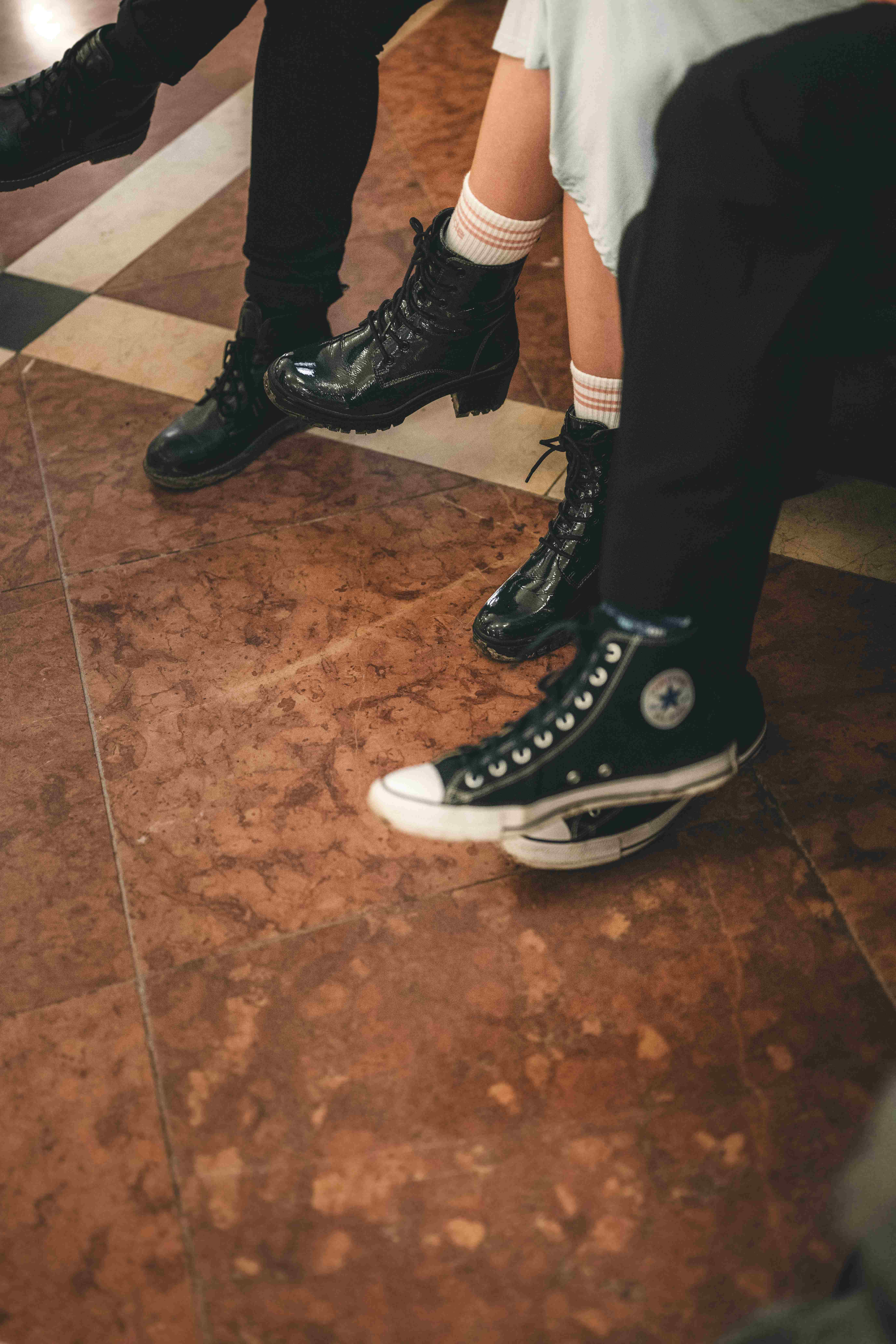 Nahaufnahme der Füße von Hochzeitsgästen auf dem historischen Fliesenboden des Rathauses, die lässige Chucks und derbe Lederstiefel zum Festkleid tragen.