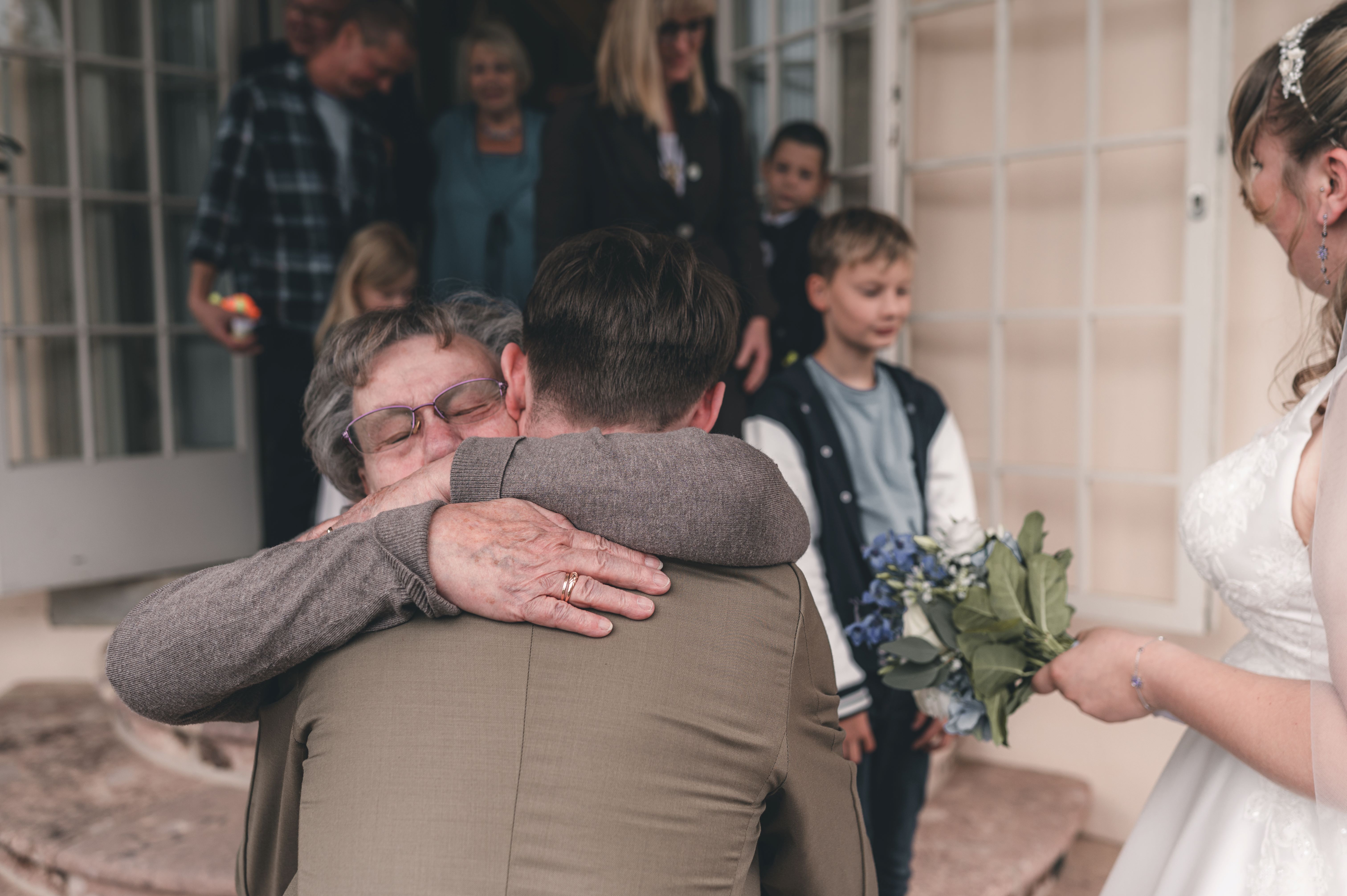 Eine ältere Verwandte drückt den Bräutigam während der herzlichen Gratulationen vor dem Schloss Lichtenwalde ganz fest an sich.