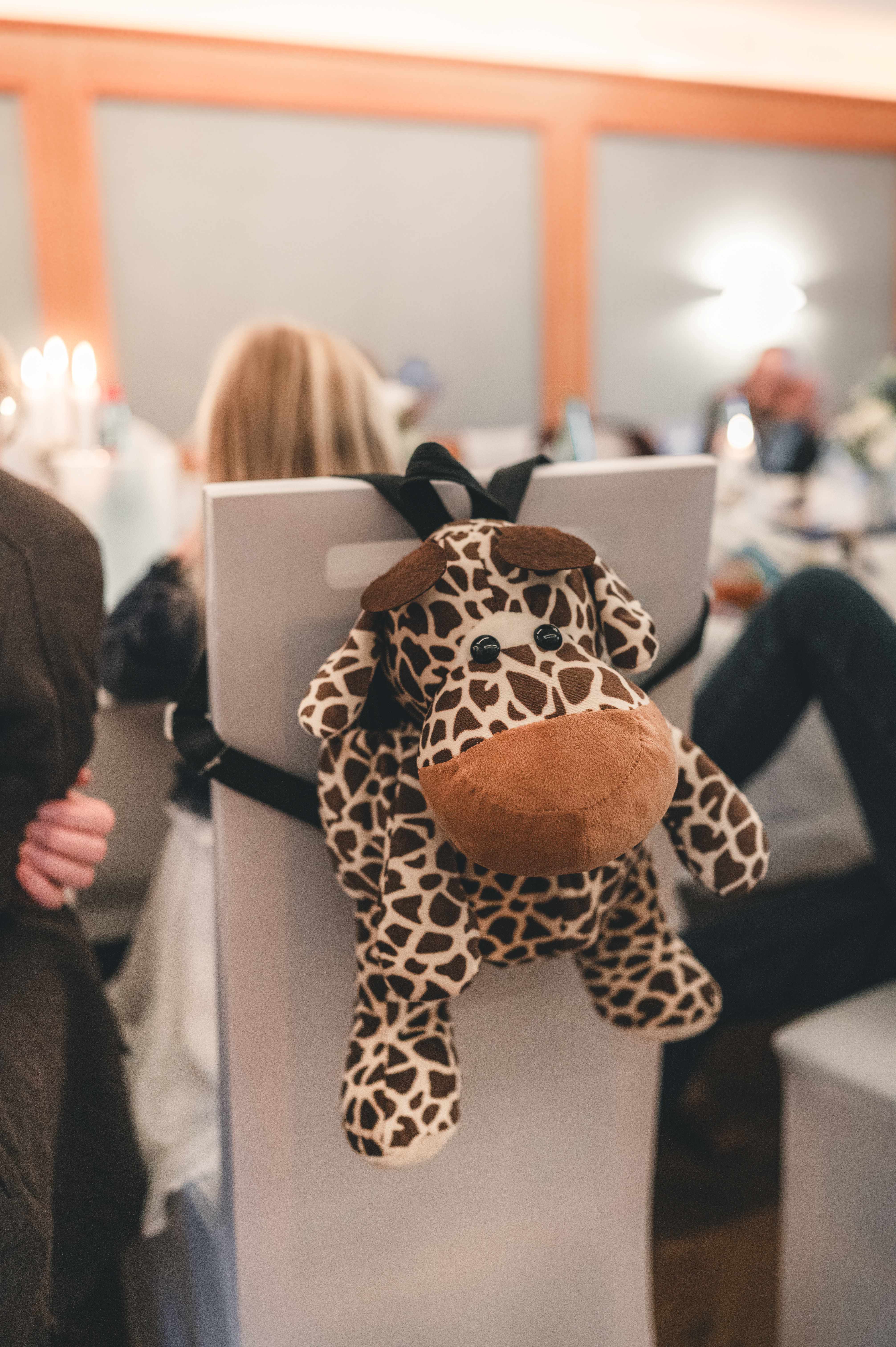 Ein plüschiger Giraffen-Kinderrucksack hängt an einer weißen Stuhllehne im Festsaal des Schlossgasthauses Lichtenwalde.