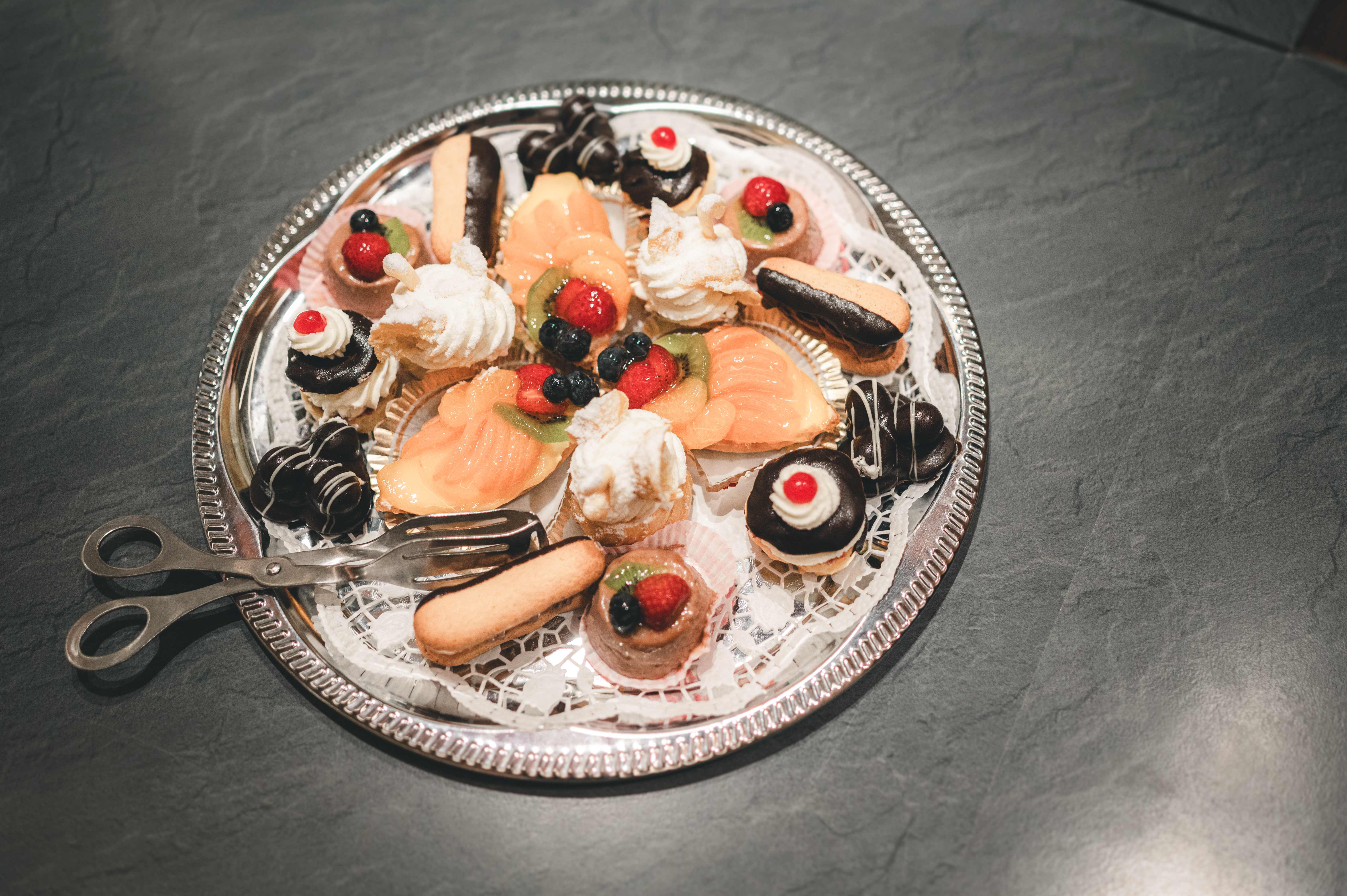 Eine silberne Servierplatte reich bestückt mit feinen Petit Fours, Fruchttörtchen und Eclairs für das Kuchenbuffet im Raum Chemnitz.