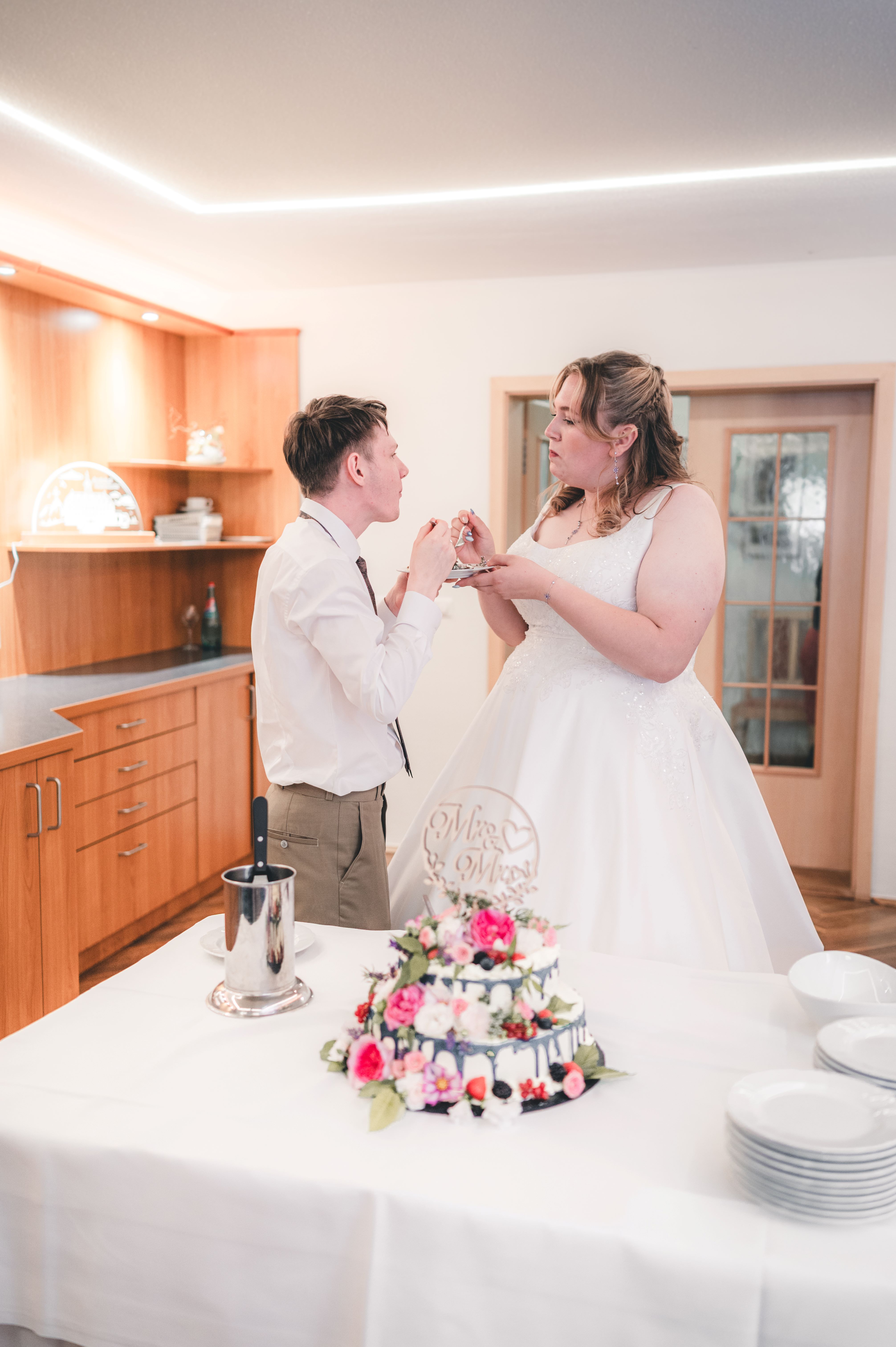 Braut und Bräutigam probieren schmunzelnd das erste Stück ihrer Hochzeitstorte im festlich beleuchteten Saal nahe Chemnitz.