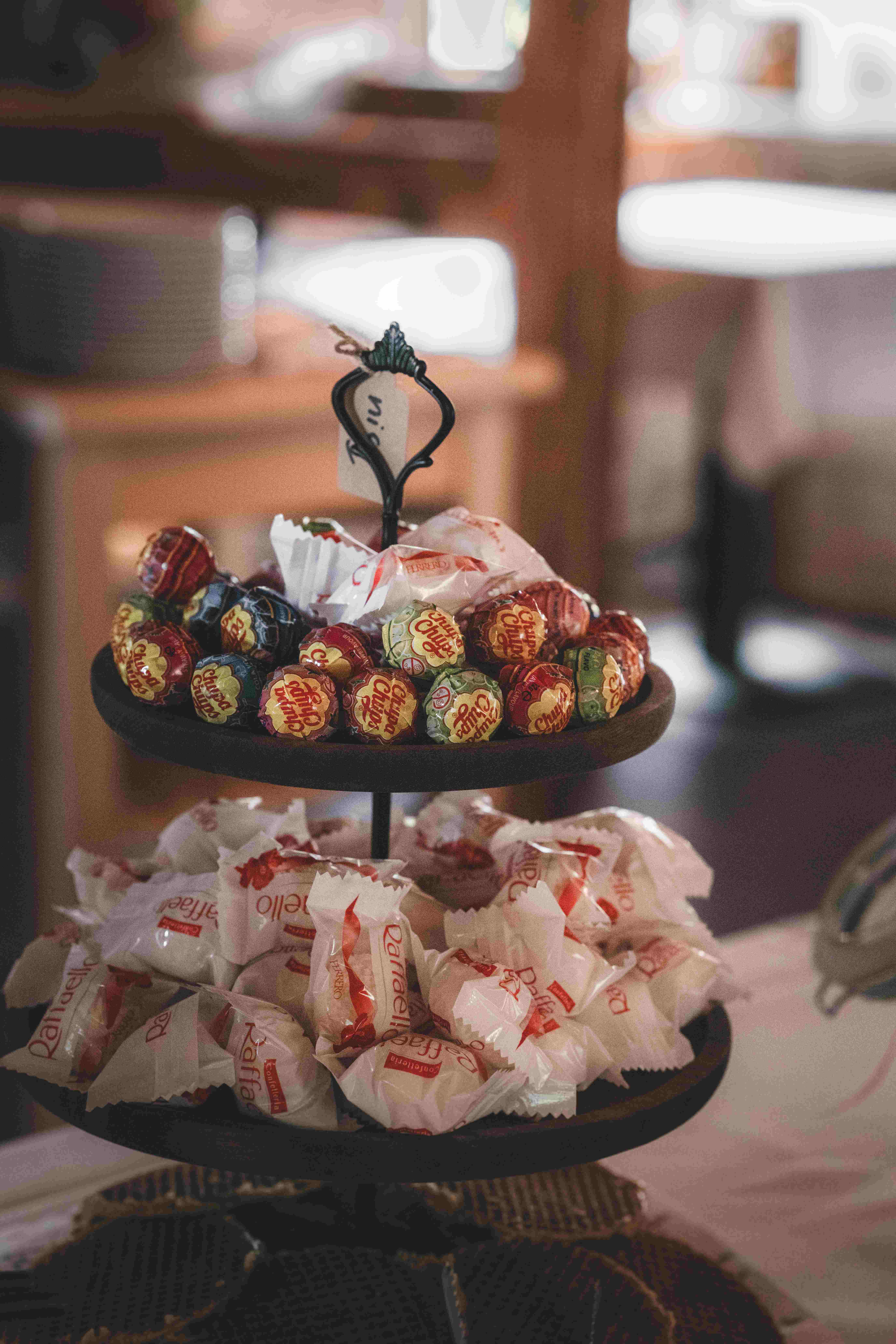 Eine zweistöckige Etagere gefüllt mit bunten Lollis und Pralinen als Teil einer liebevoll gestalteten Candybar bei der Hochzeitsfeier.