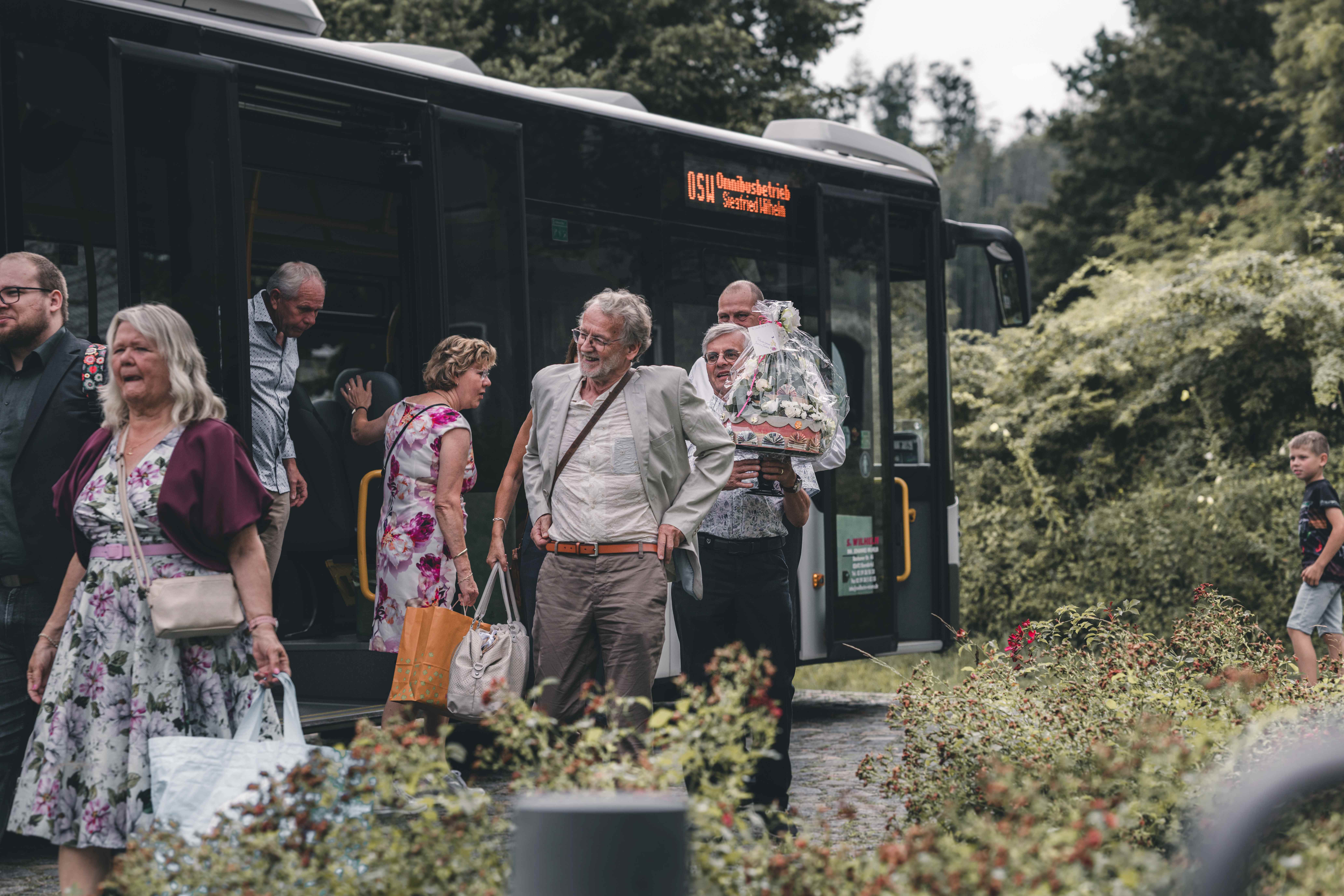 Gut gelaunte Hochzeitsgäste steigen aus einem Linienbus an der Alten Schäferei in Oppach aus und bringen Geschenke zur Feier mit.