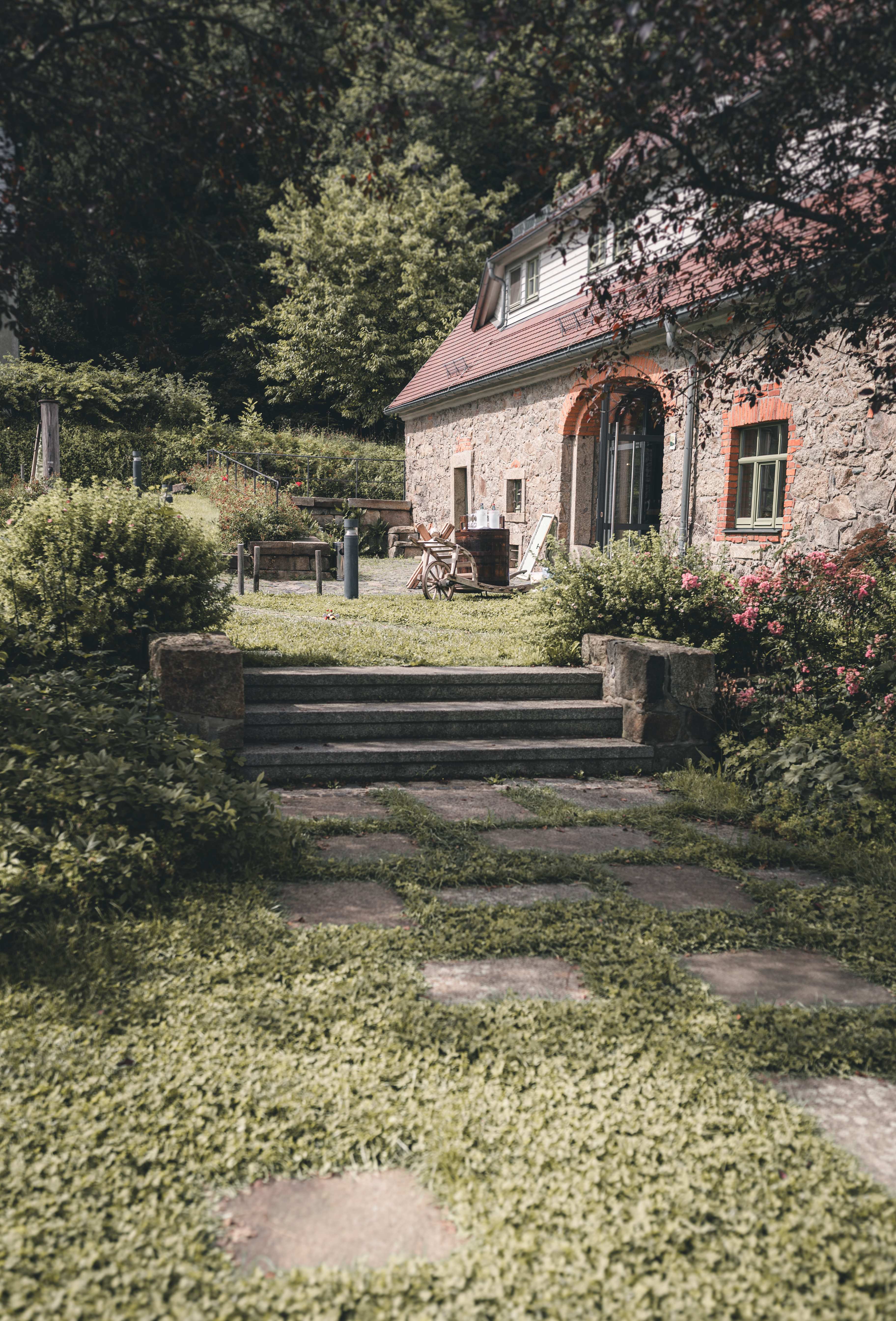 Die grüne Gartenterrasse der Alten Schäferei Oppach mit Natursteinstufen und liebevoll angelegten Blumenbeeten im Sommer.
