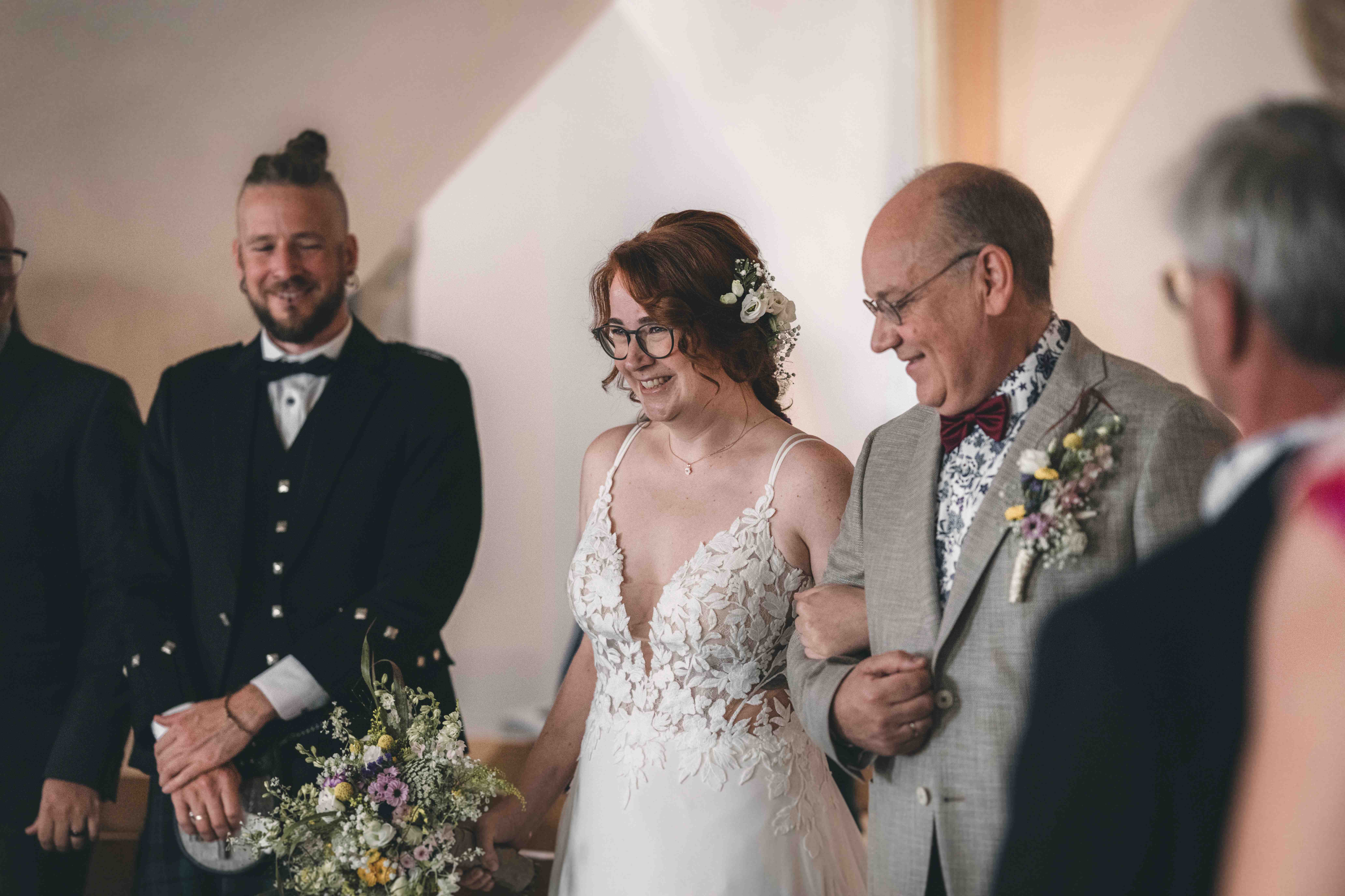 Der Brautvater führt seine Tochter im weißen Hochzeitskleid unter den Blicken der Gäste zum wartenden Bräutigam im Standesamt Pirna.