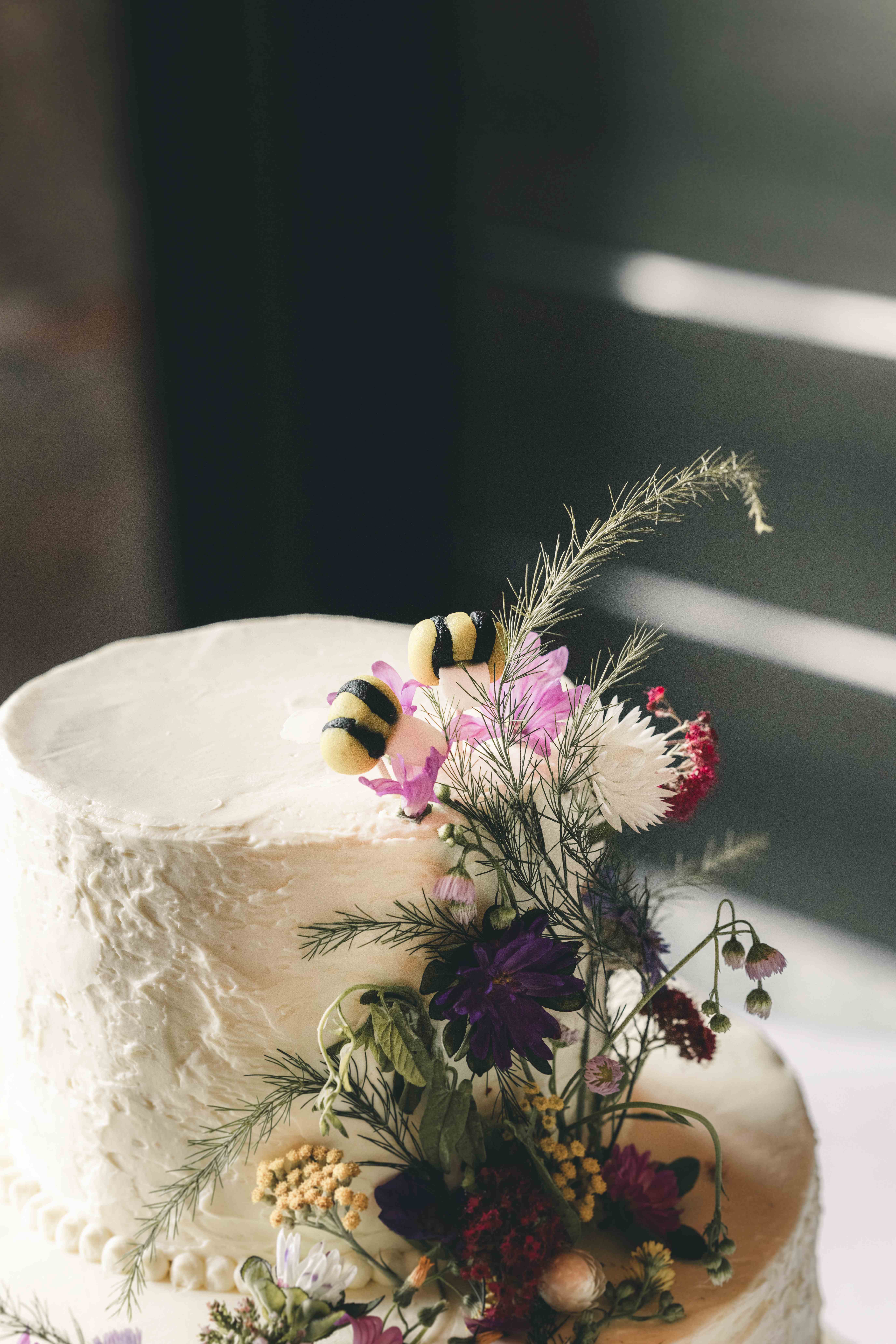 Nahaufnahme der oberen Etage einer Hochzeitstorte mit bunten Blüten und zwei kleinen, süßen Deko-Bienen als Tortenfigur in Sachsen.