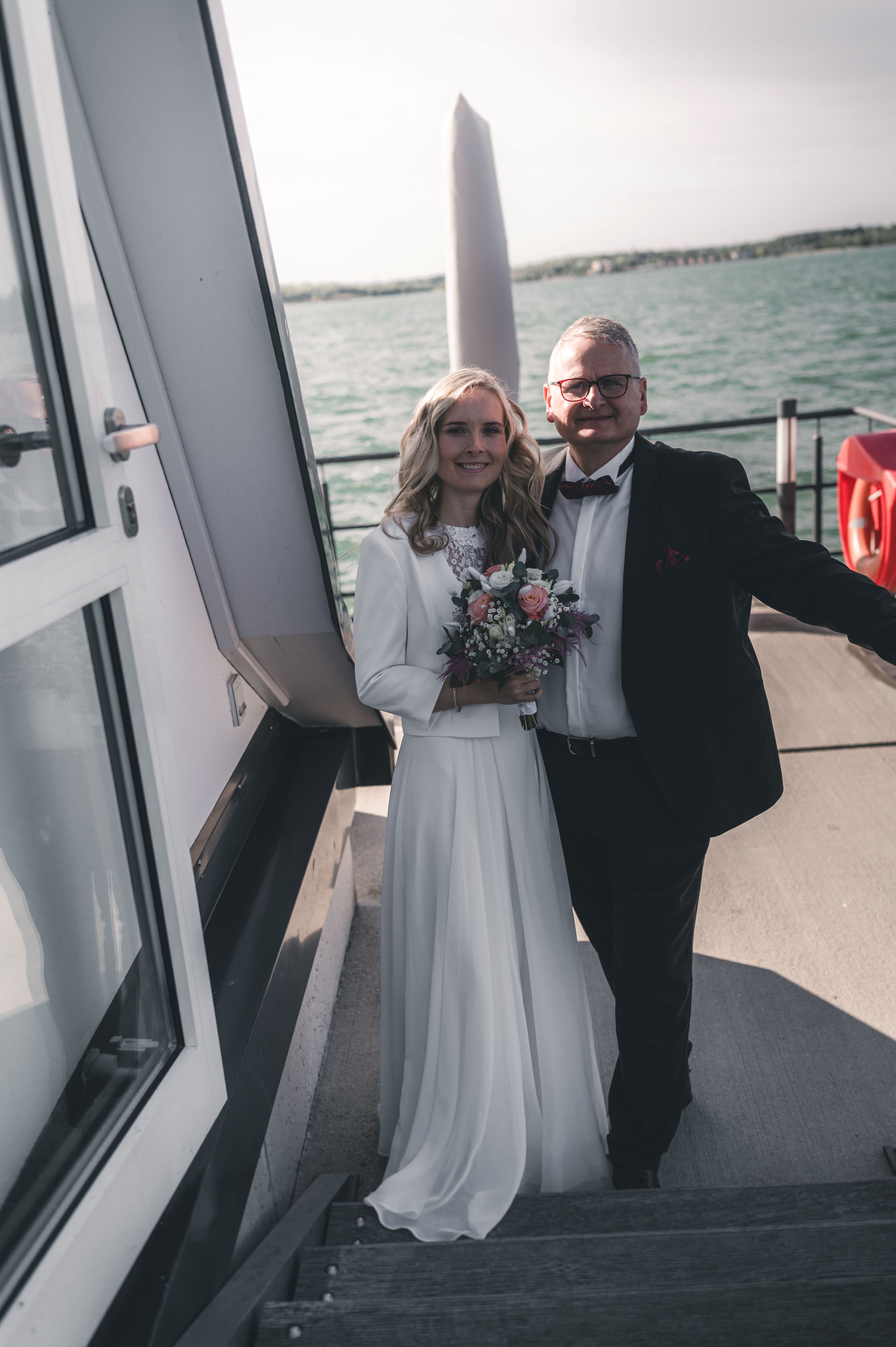 Die Braut im weißen Kleid steht mit dem Brautvater an den Stufen des Bootes direkt nach dem Anlegen an der VINETA.
