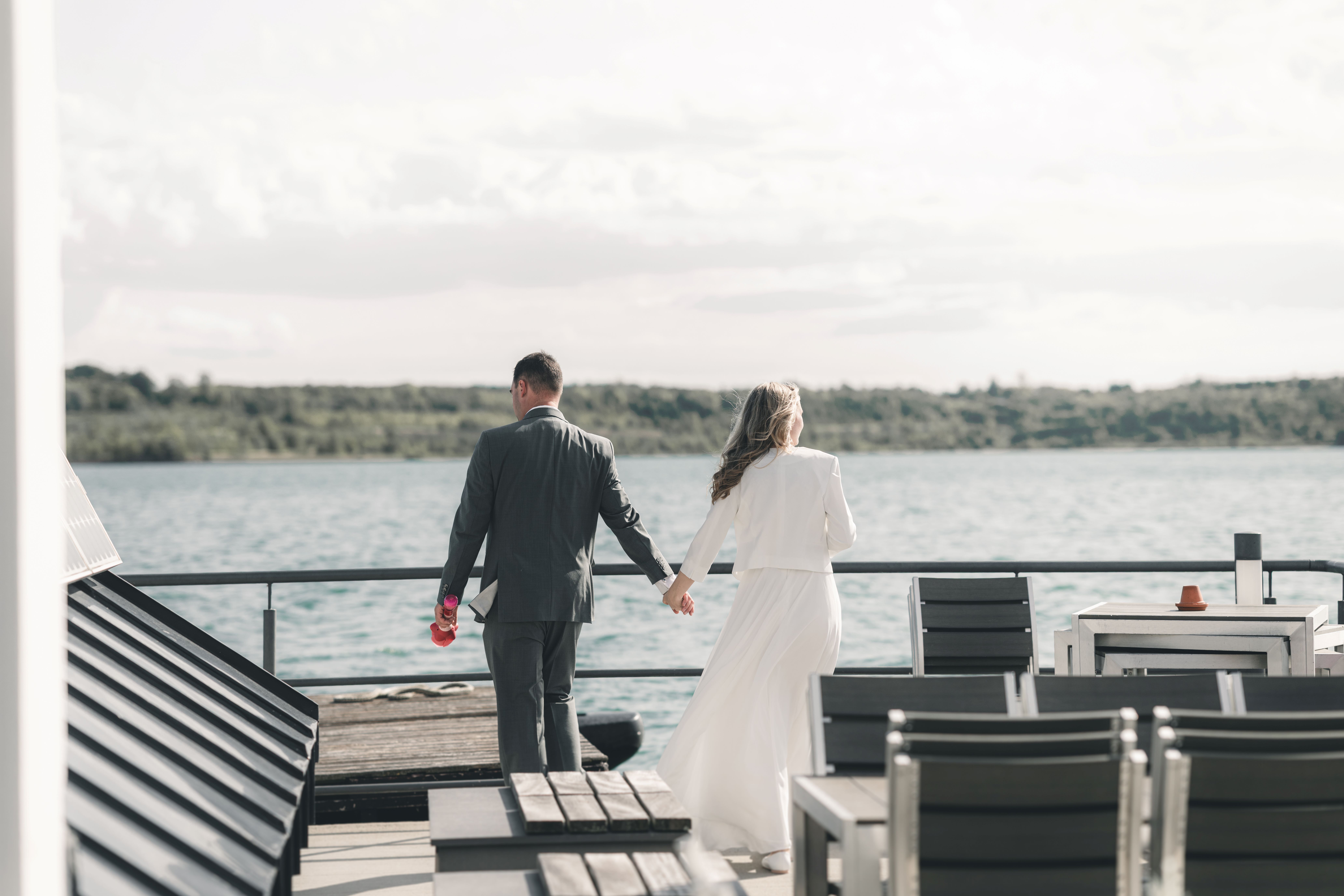Das Brautpaar läuft Hand in Hand über das Außendeck der VINETA mit Blick auf das weite Wasser des Störmthaler Sees.