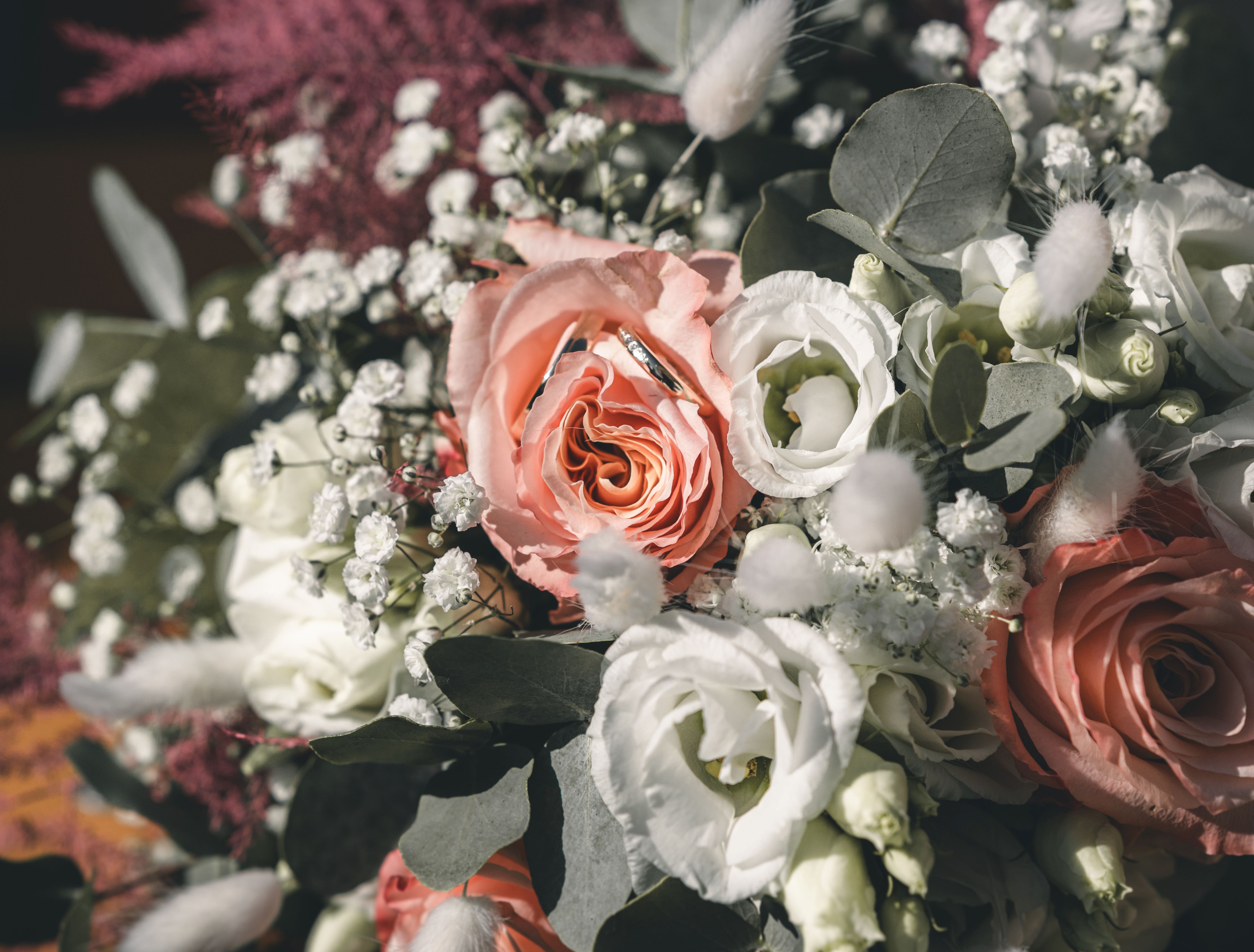Nahaufnahme der goldenen Eheringe, die elegant in den zarten Blüten einer rosa Rose im sommerlichen Brautstrauß platziert sind.