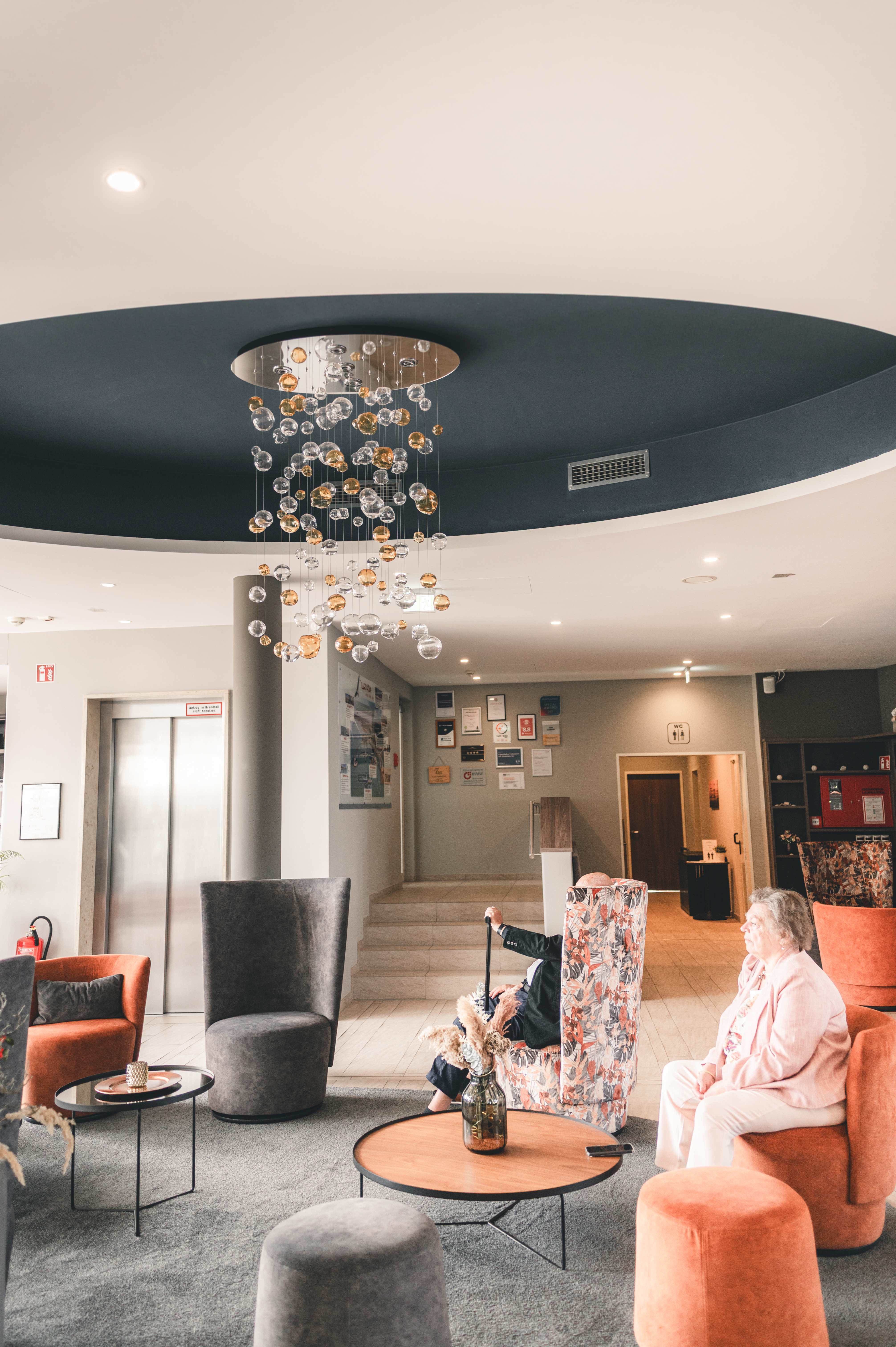 Die geschmackvoll eingerichtete Lobby des Hotels Lagovida am Störmthaler See mit gemütlichen Sesseln und einem modernen, gläsernen Kronleuchter.